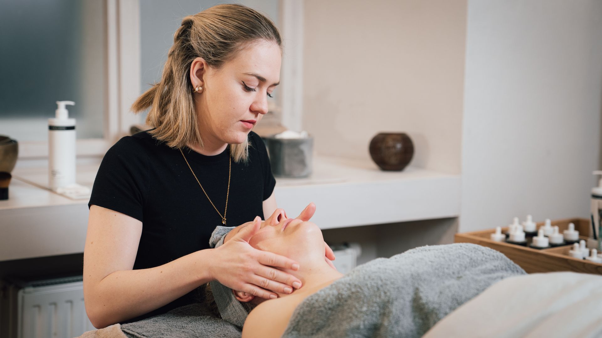 Eine Kosmetikerin gibt einer Kundin auf einer Behandlungsliege in einem Spa-Raum eine Gesichtsmassage.