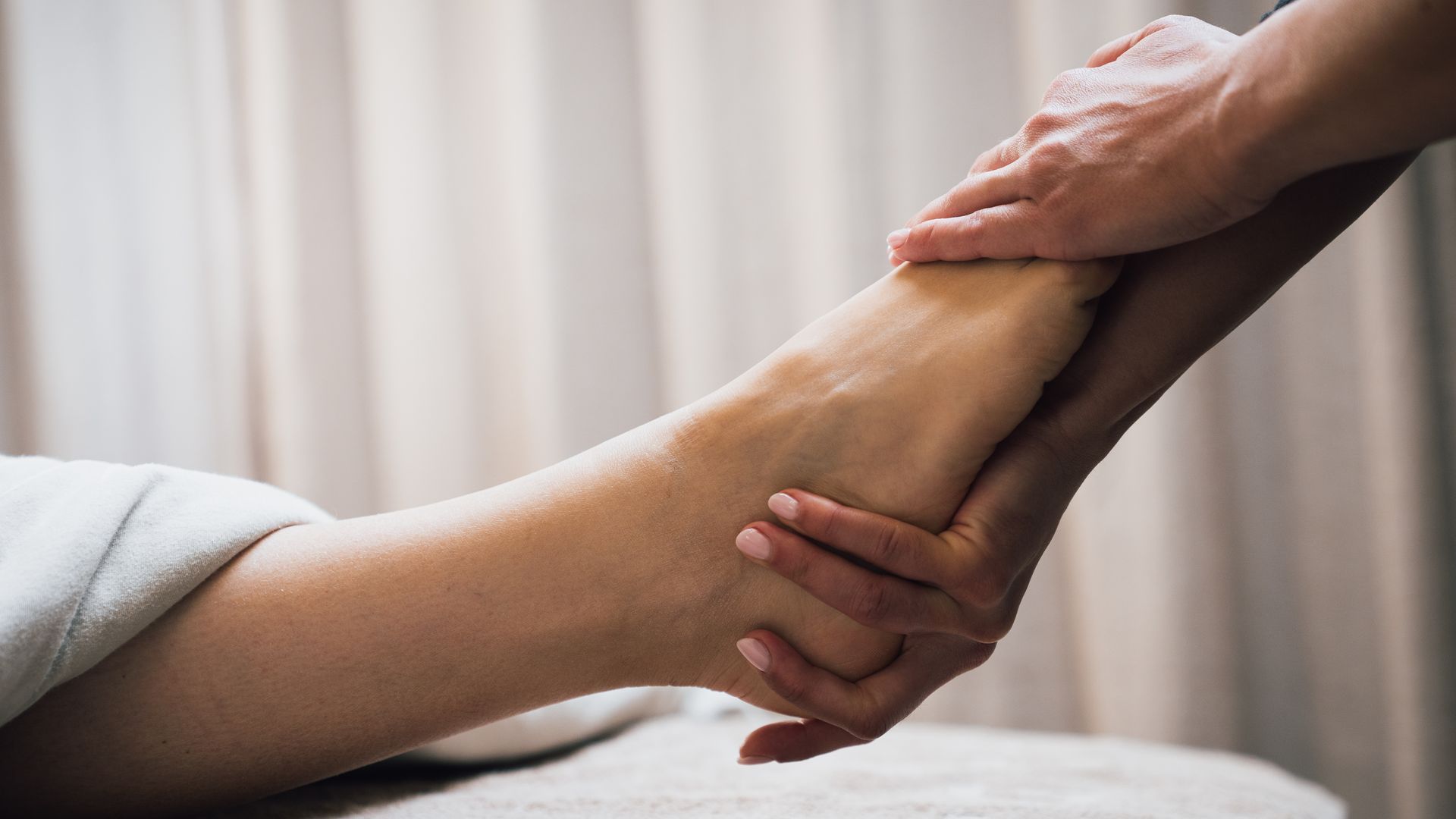 Hände, die während einer Massage auf einem Bett sanft den Knöchel einer Person halten.