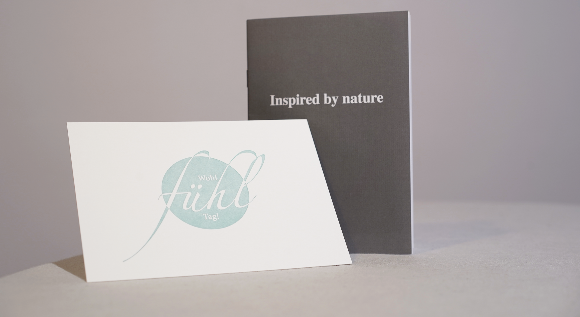Zwei minimalistische Grußkarten, weiß und dunkelgrau, auf hellem Untergrund; auf einer steht „Von der Natur inspiriert“.
