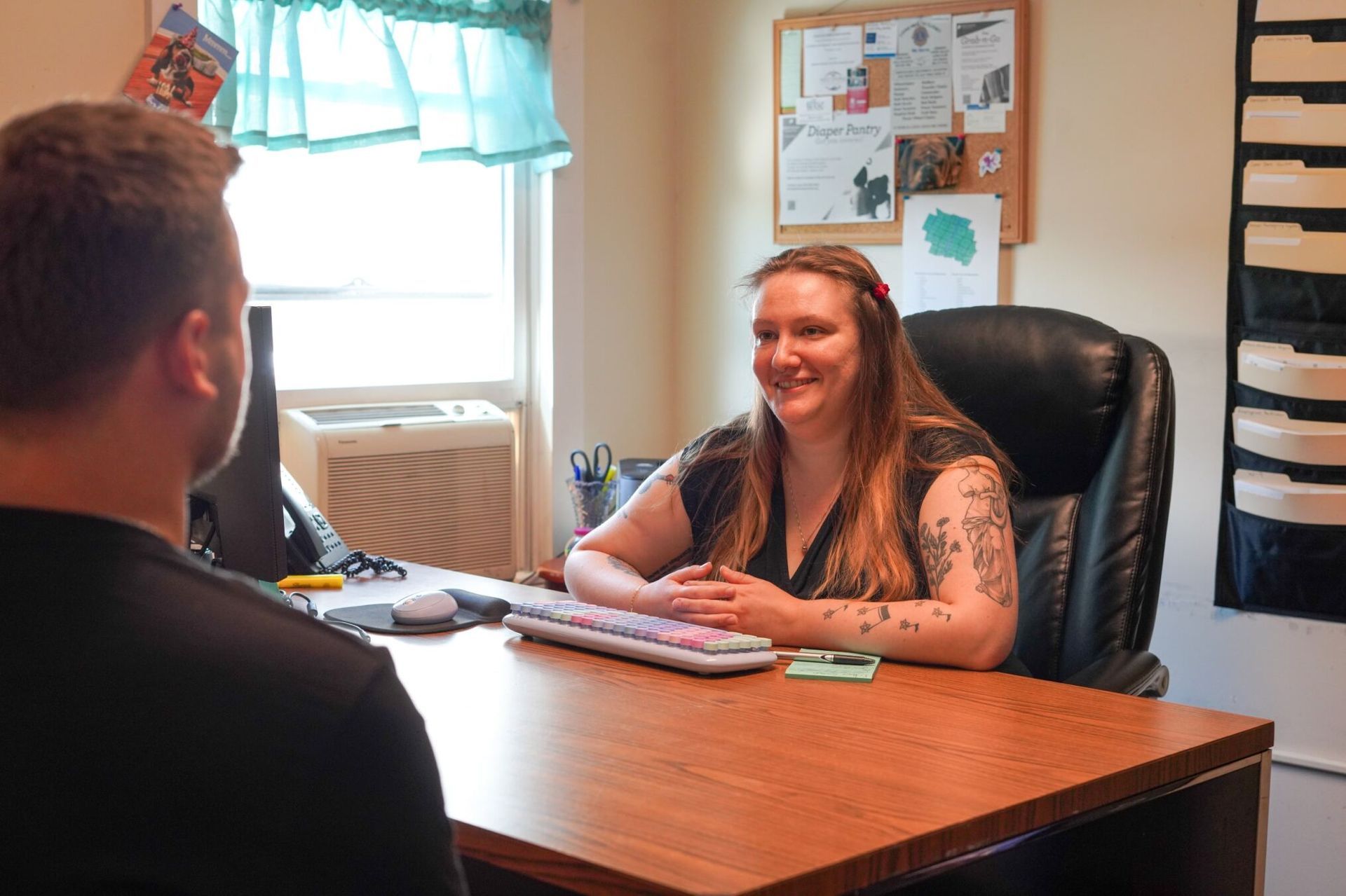 A woman is sitting at a desk talking to a man.