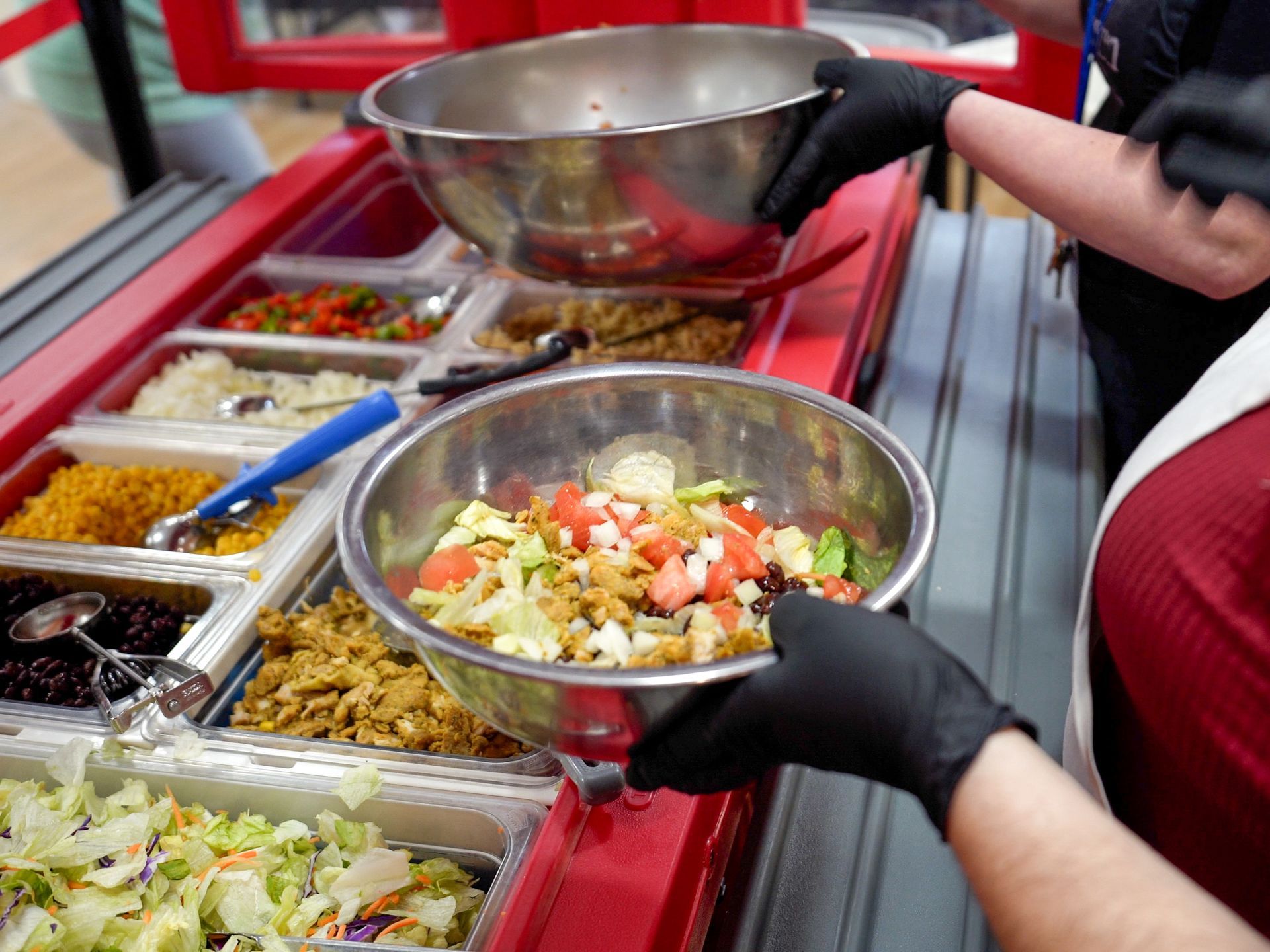 A person wearing black gloves is holding a bowl of food.