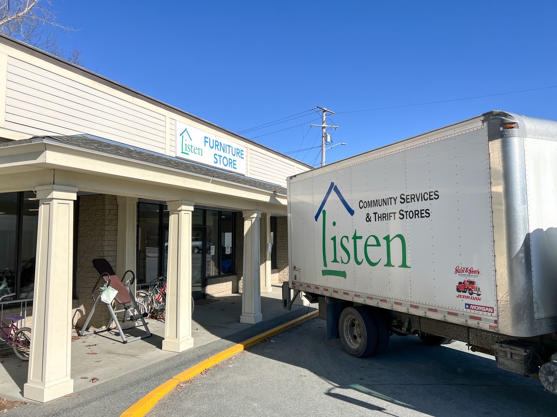 A white truck with the word listen on the side is parked in front of a building.