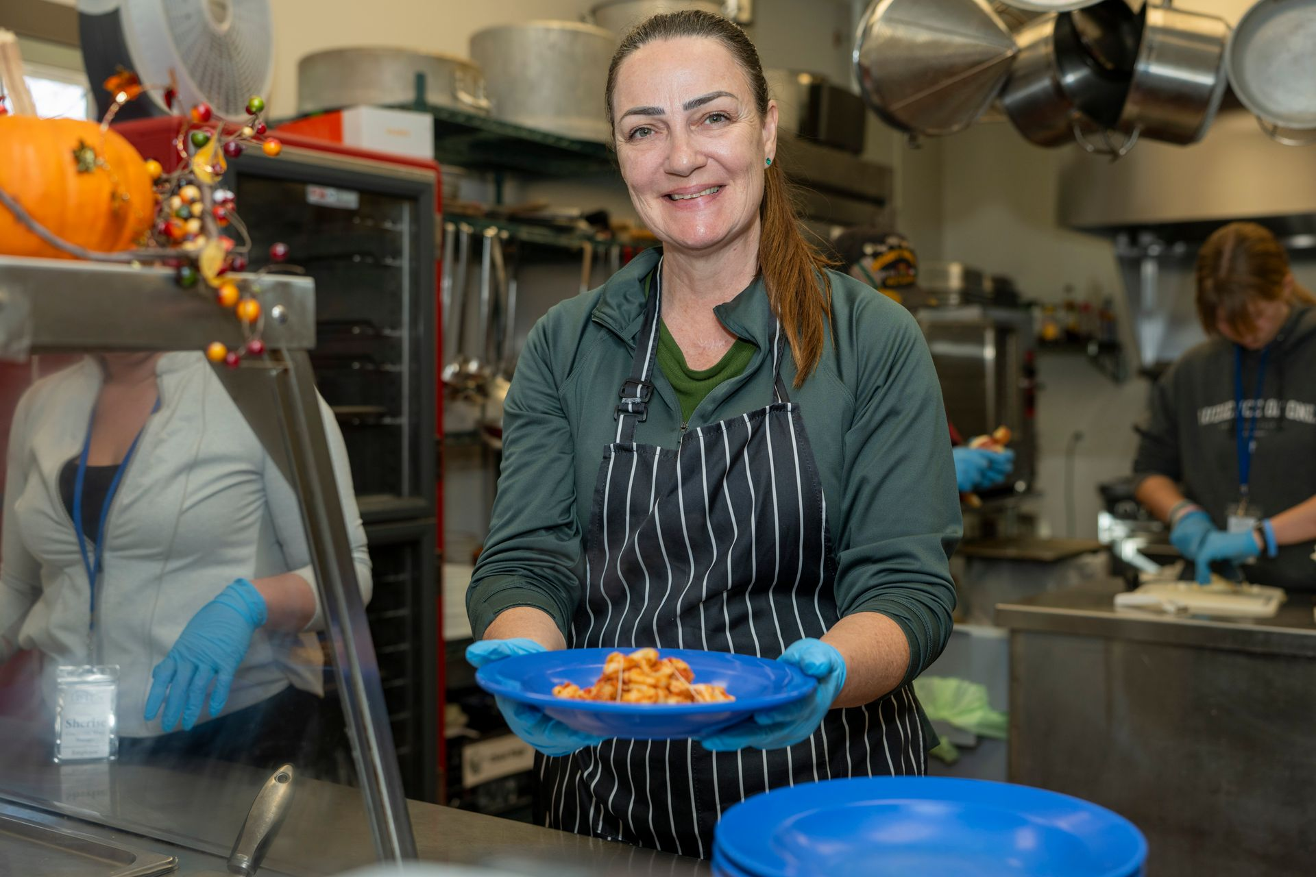 Chef in striped apron serving food in a busy commercial kitchen with a blue plate