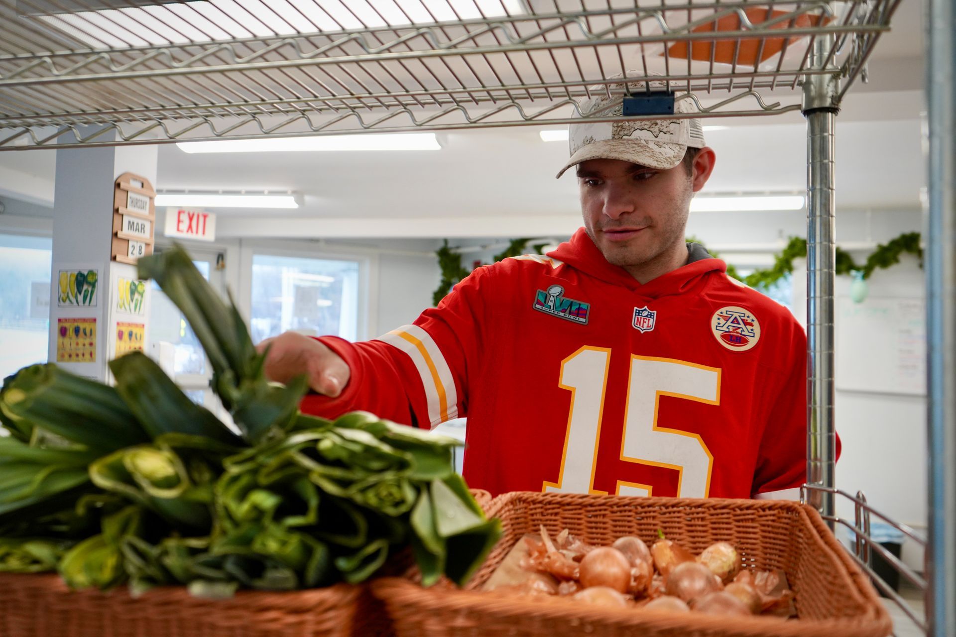 A man in a chiefs jersey is picking vegetables from a shelf.