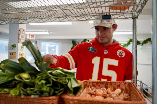 A man in a chiefs jersey is picking vegetables from a shelf.