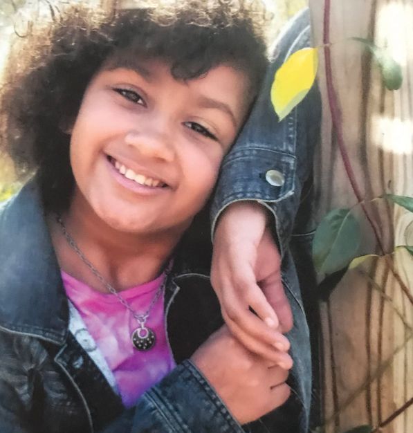 A little girl in a pink shirt and denim jacket is smiling