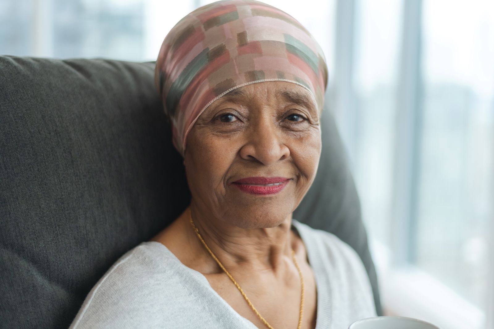 A woman with cancer is sitting in a chair with a cup of coffee.