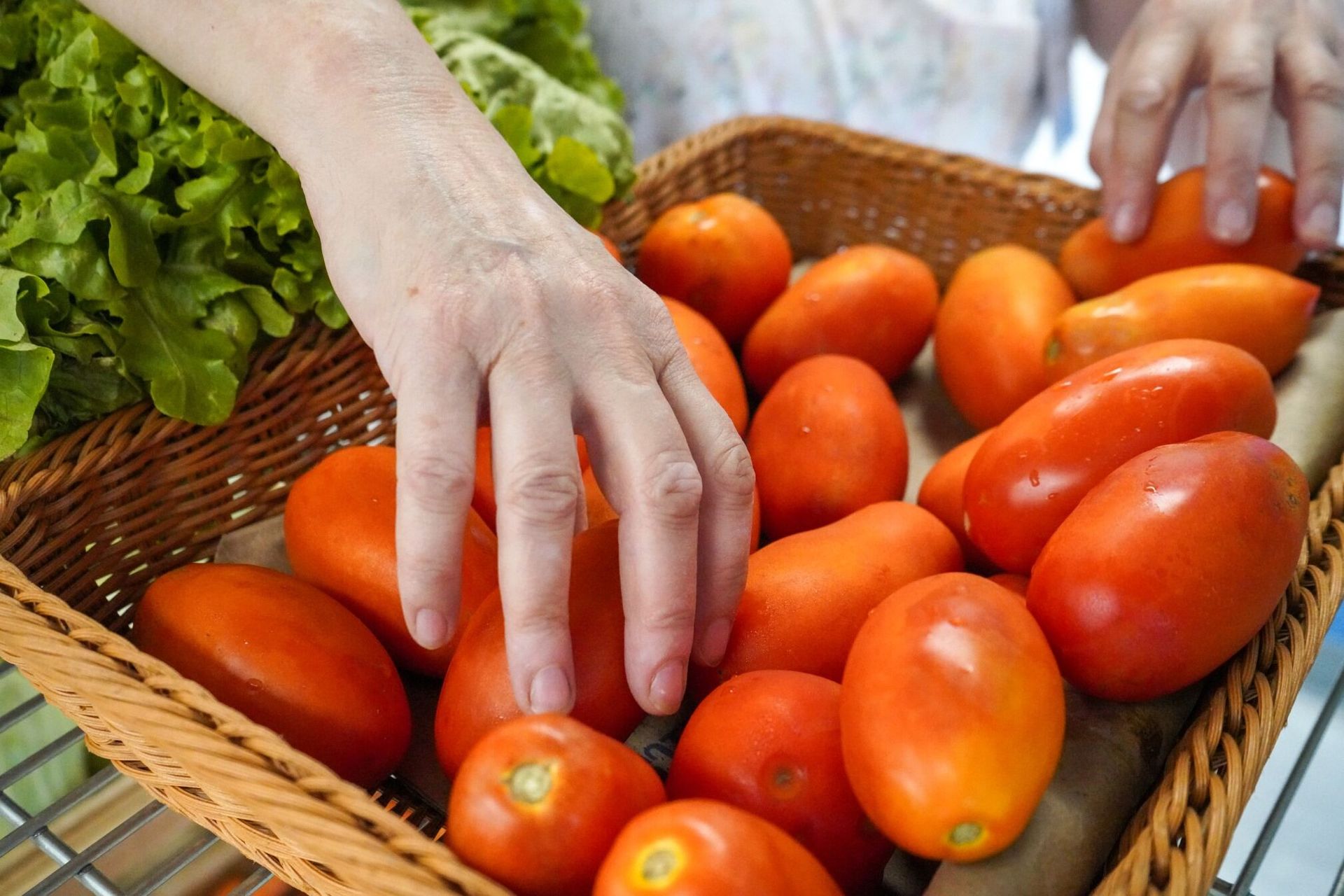 A person is picking tomatoes out of a basket.