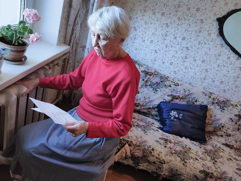 An elderly woman is sitting on a couch reading a letter