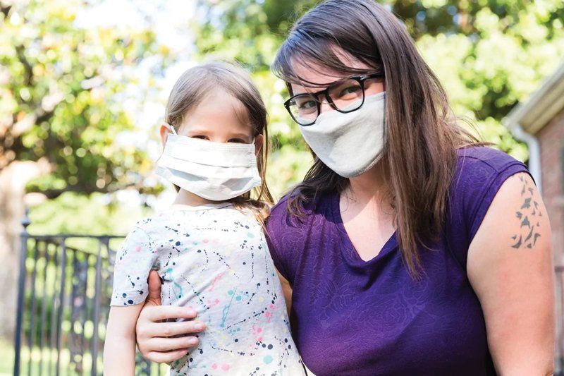 A woman wearing a face mask is holding a little girl.