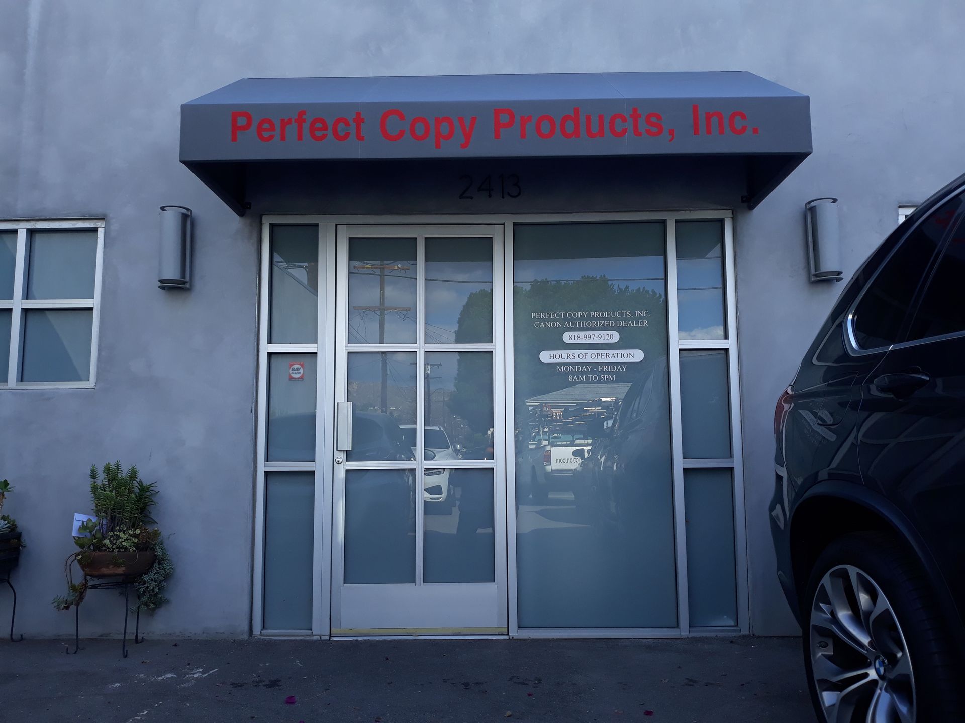 Storefront of Perfect Copy Products, Inc. with glass door and gray awning; black SUV parked at right.