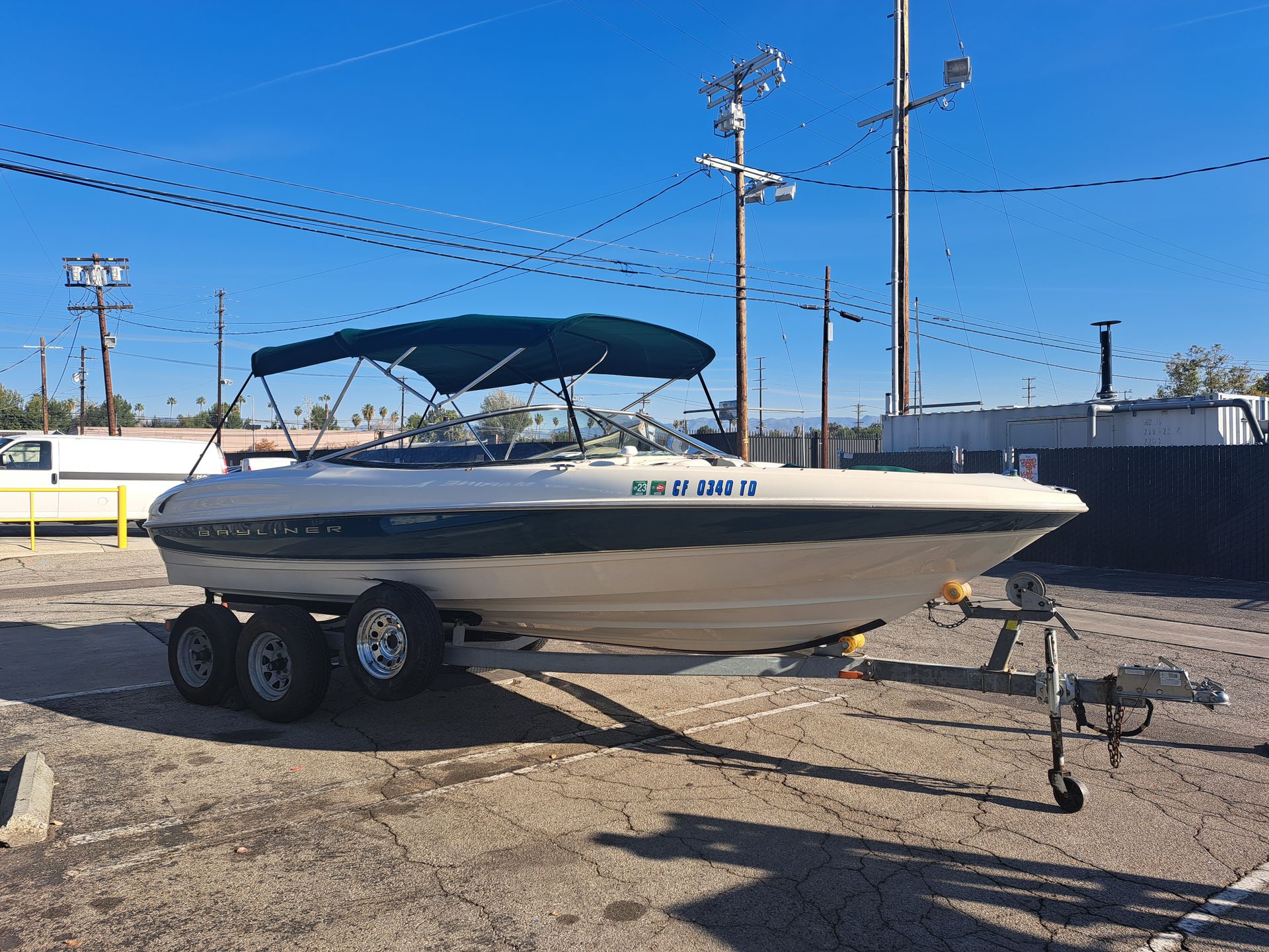 White speedboat on a trailer in a sunny lot, with a blue bimini top and clear sky.