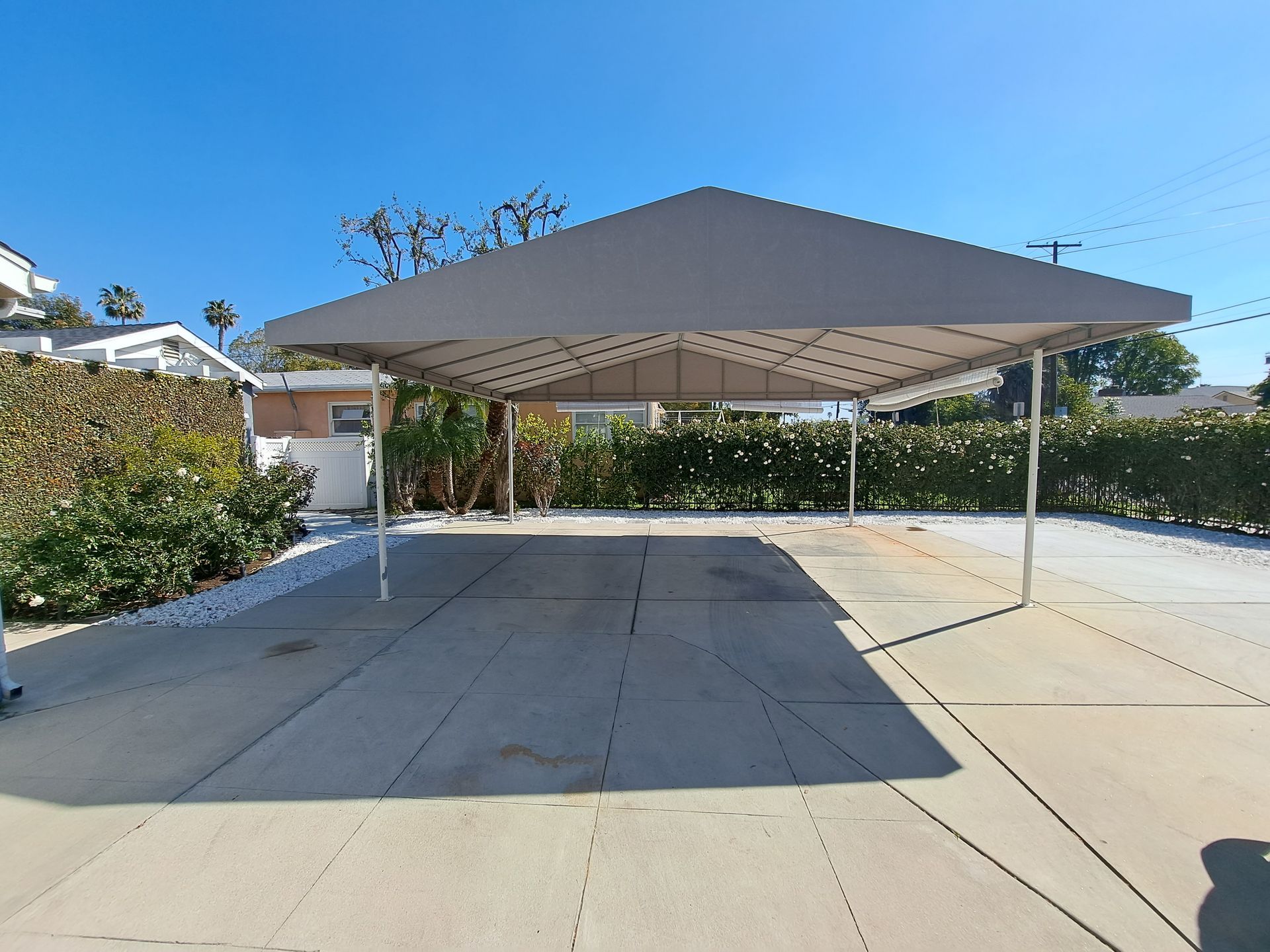 Large beige carport canopy over a concrete driveway, with trees and blue sky in the background