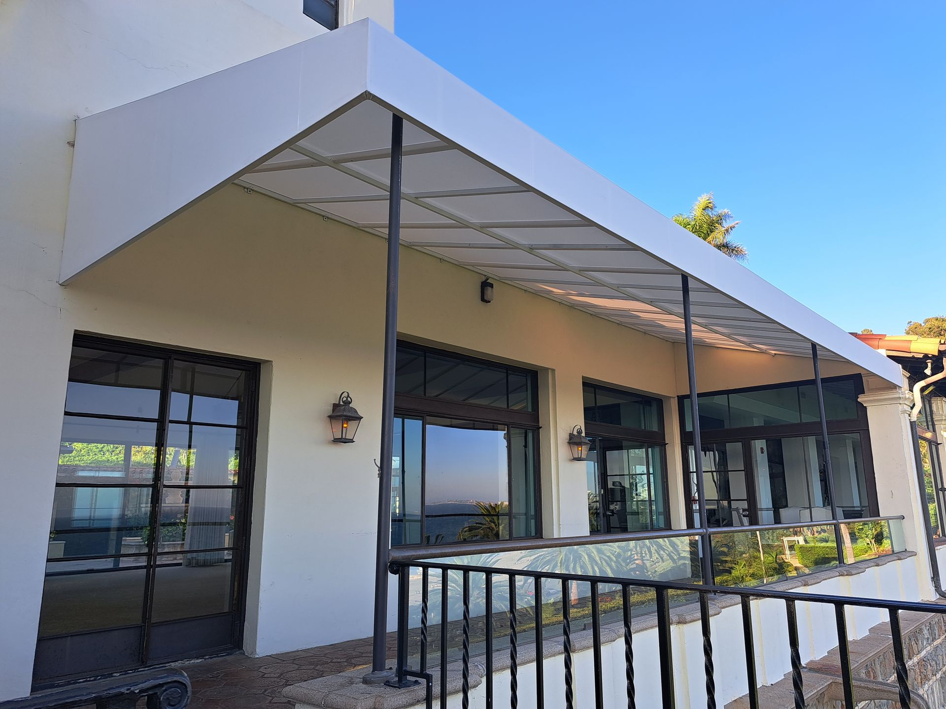 Modern building exterior with white walls, black railings, and a covered patio under a blue sky