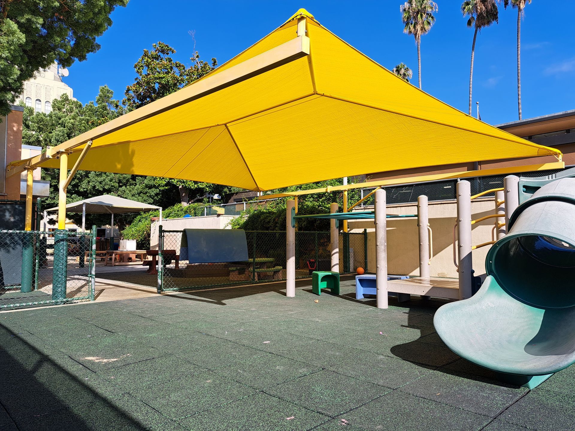 Yellow shade sail over a playground with climbing equipment and a large slide on a sunny day