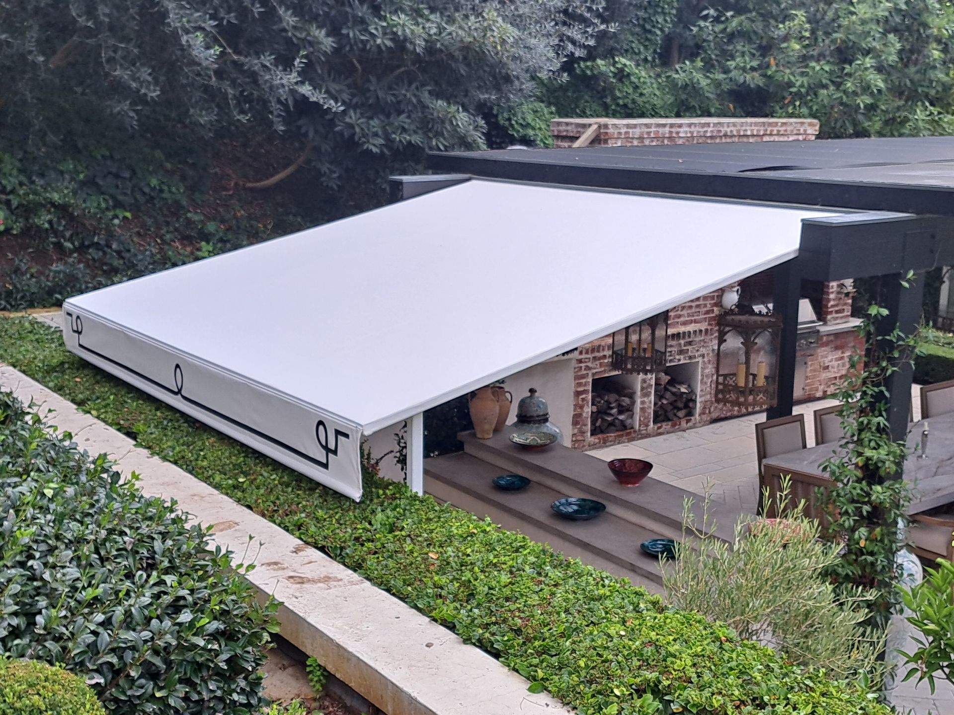 Modern house with large white flat roof and open patio on a hillside, surrounded by greenery