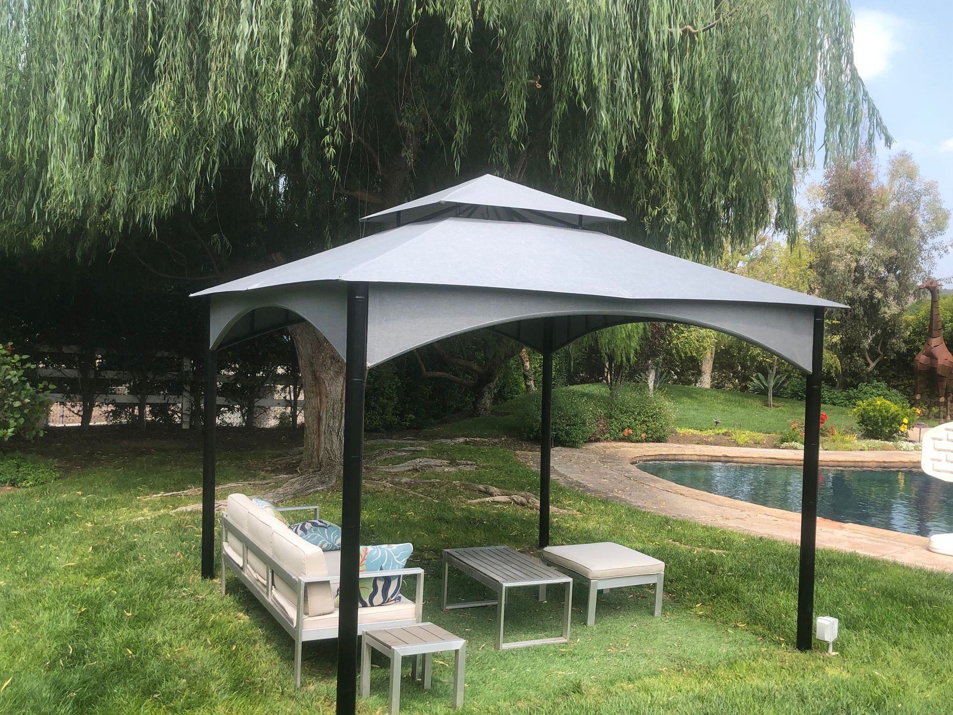 Covered patio gazebo beside a backyard pool, with benches and a table under a gray canopy.