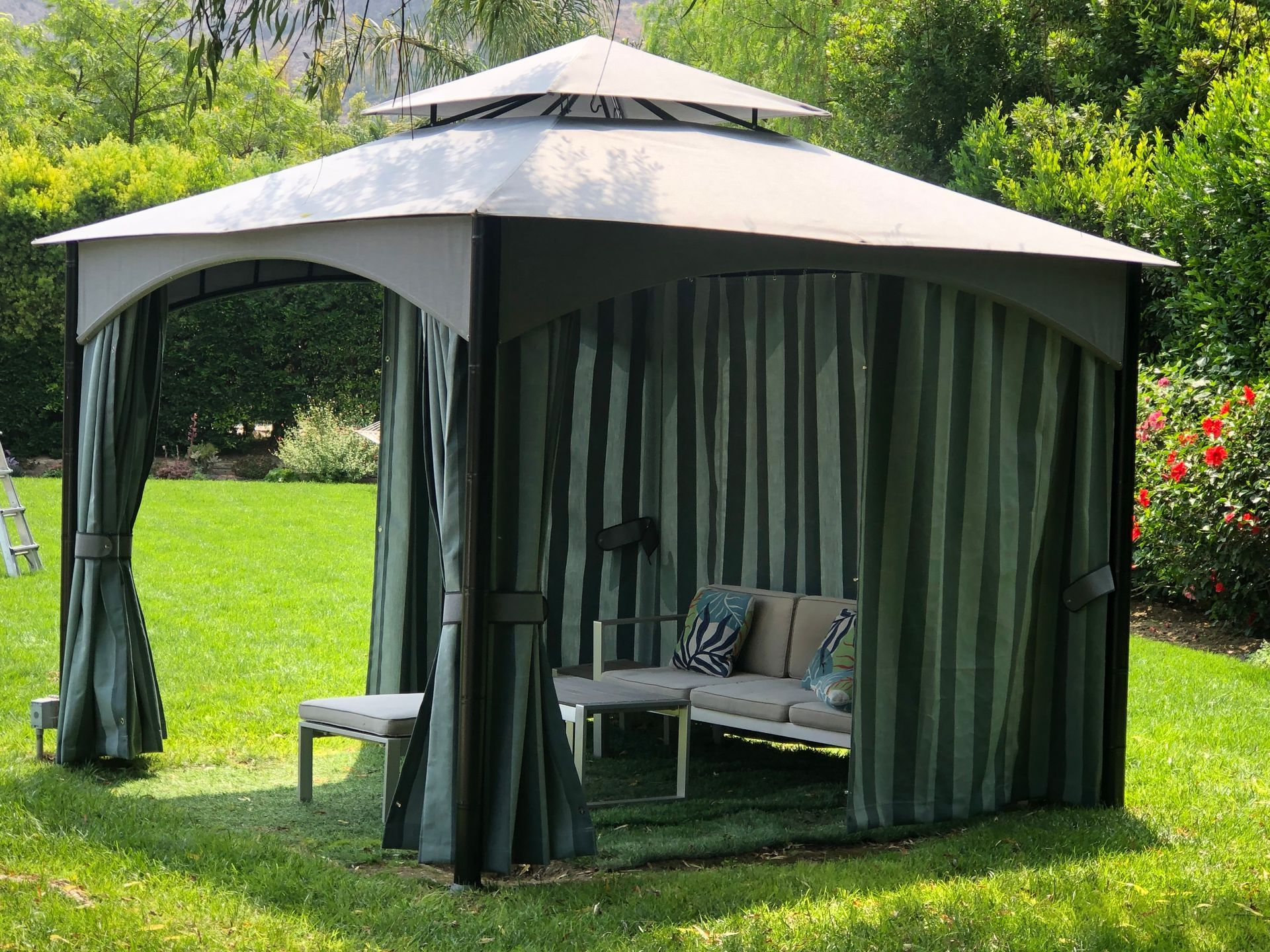 Green gazebo with striped curtains and cushioned seating in a garden