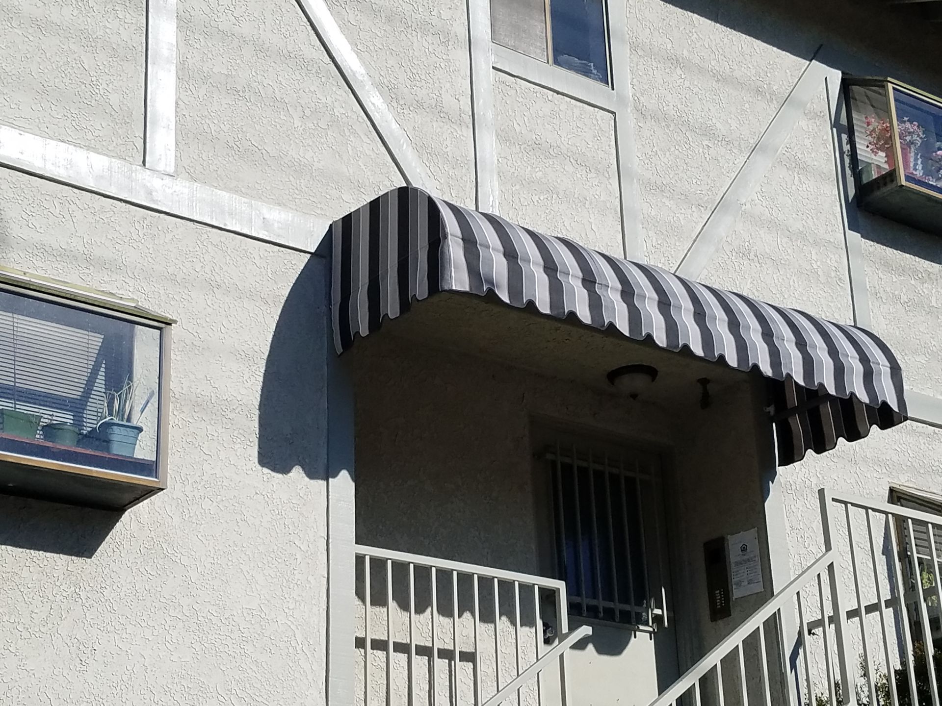 Apartment entrance with striped awning and white railing on a gray building