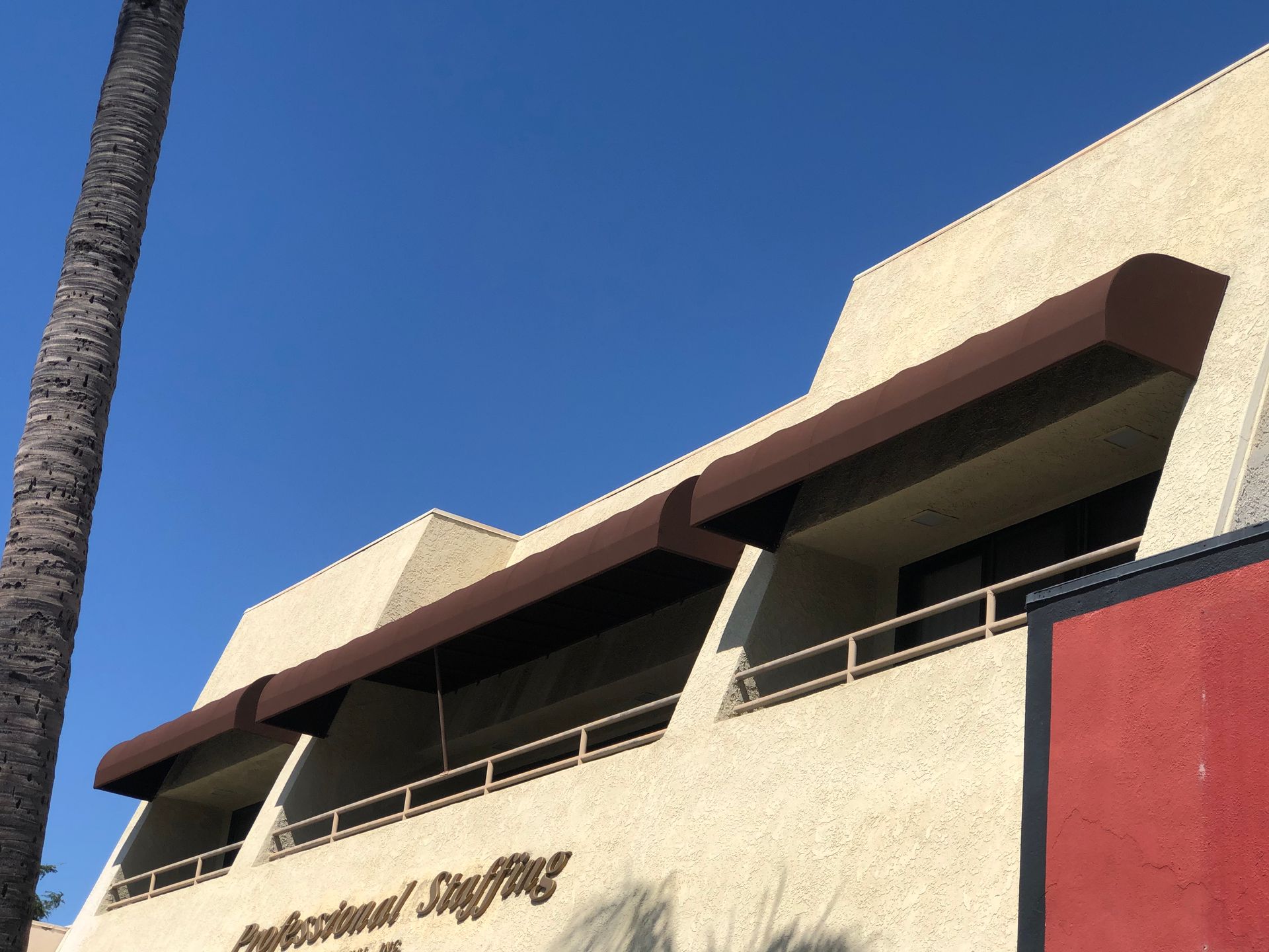 Exterior of a beige building with brown awnings and red accents against a clear blue sky
