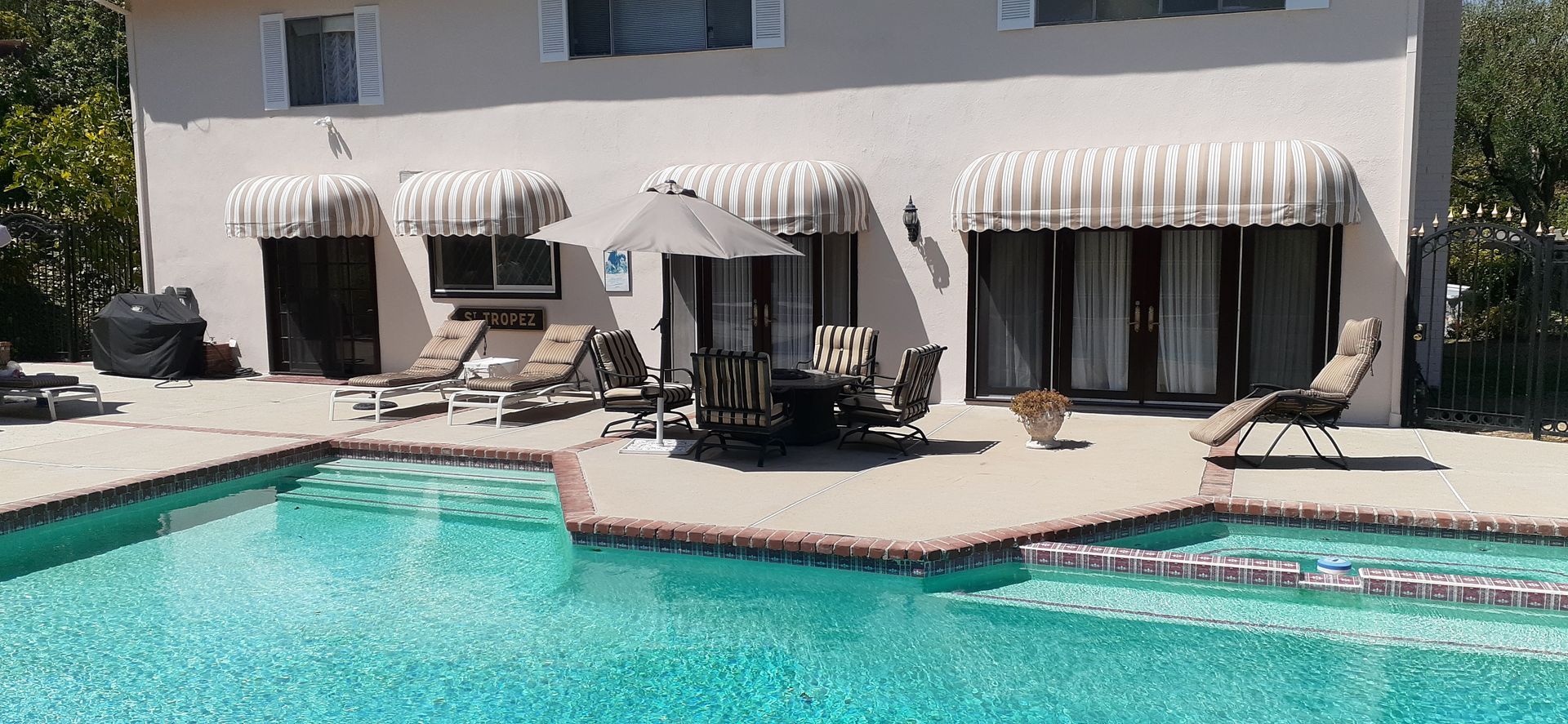 Luxury poolside patio with striped awnings, lounge chairs, and a turquoise swimming pool