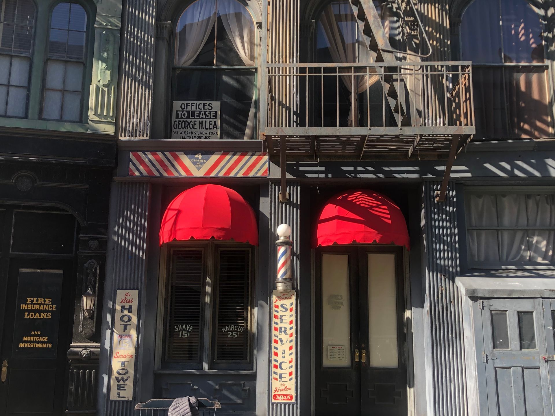 Old building facade with red awnings, tall windows, and a hanging balcony