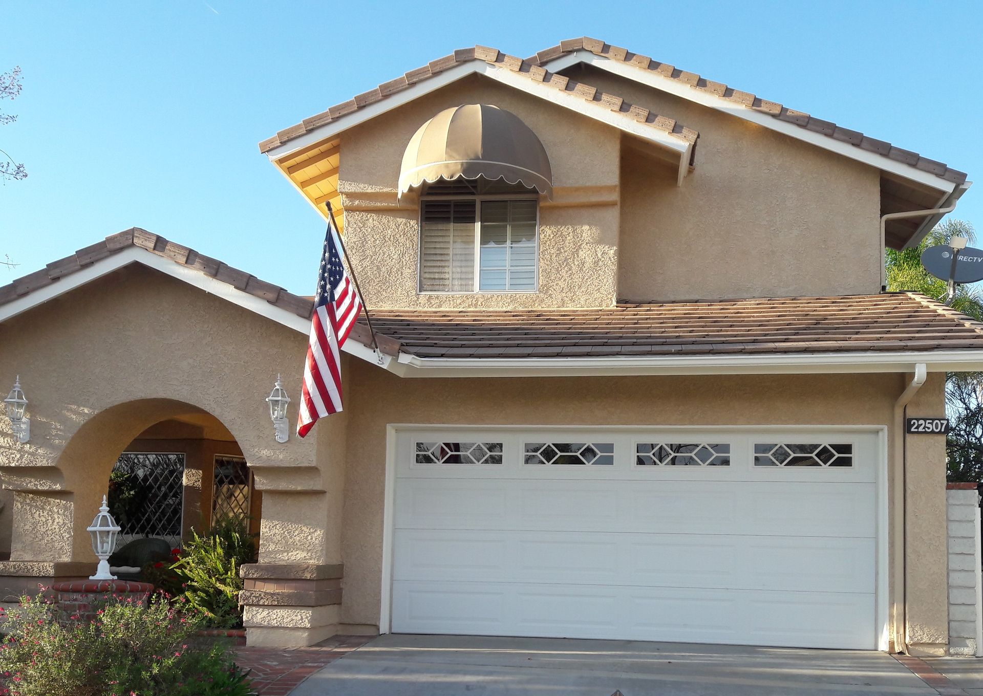 Two-story tan house with white garage door and an American flag by the front entrance