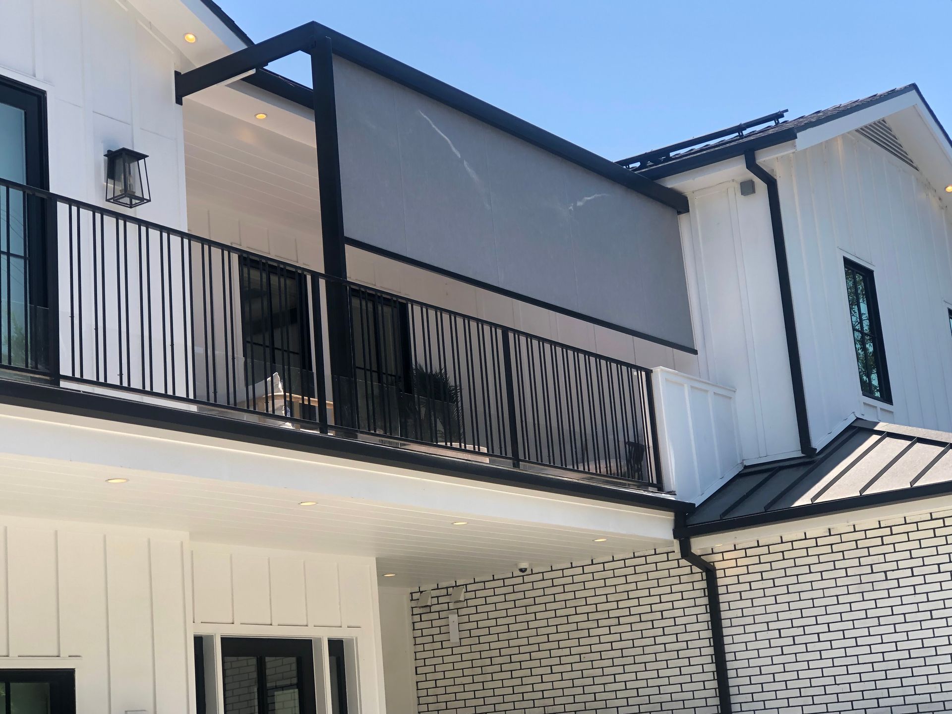 Modern white two-story house with black balcony railings and a sloped roof against a blue sky