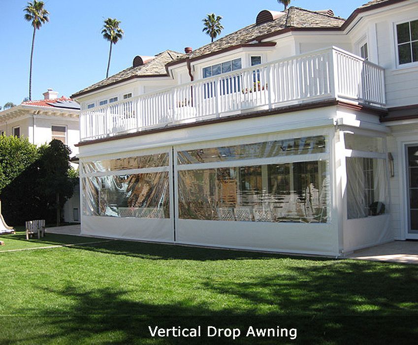 Vertical drop awning covering patio windows on a white two-story house with a green lawn