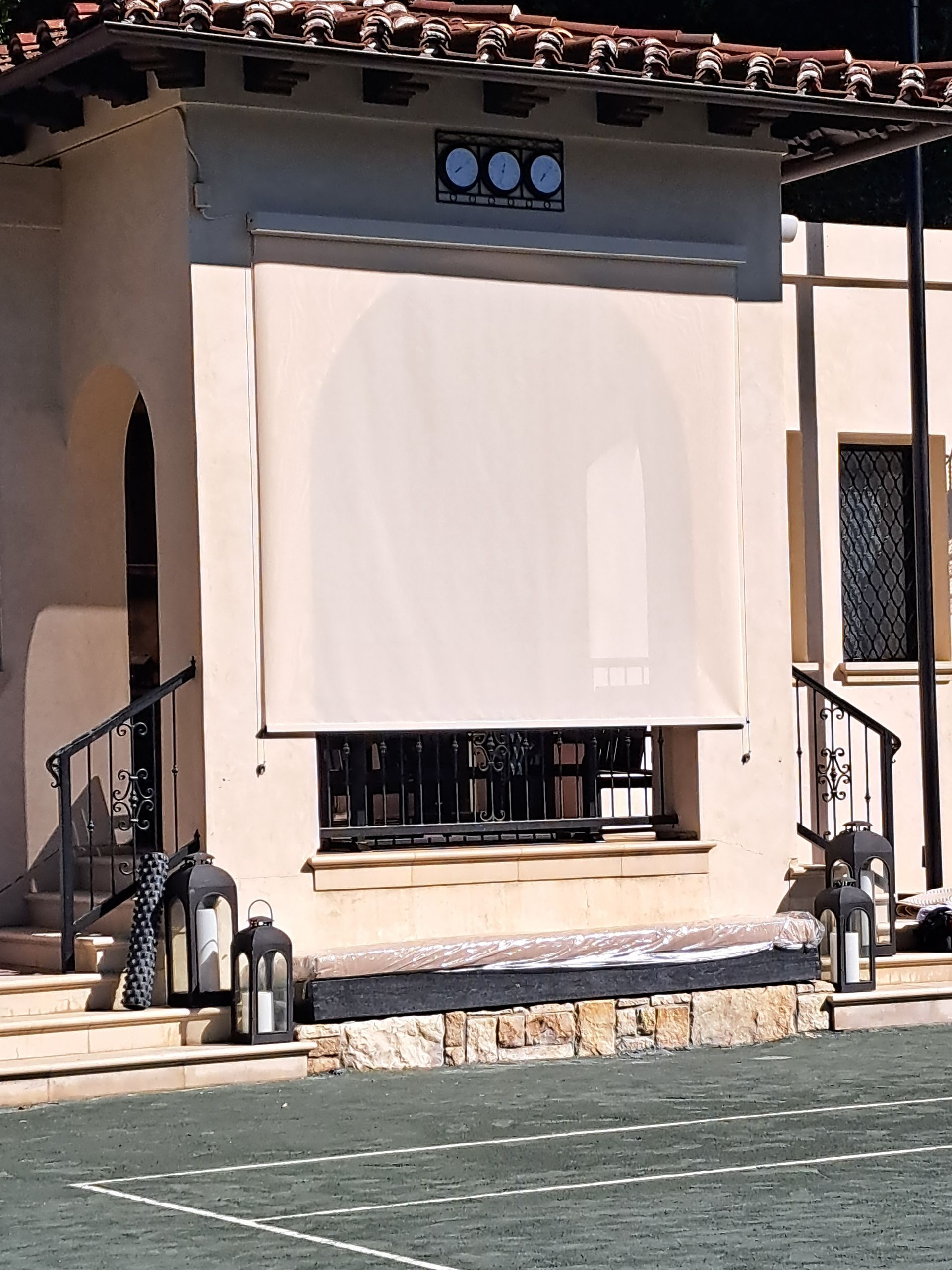 Patio with a beige stucco wall, large white shade, and small window under a tiled roof.