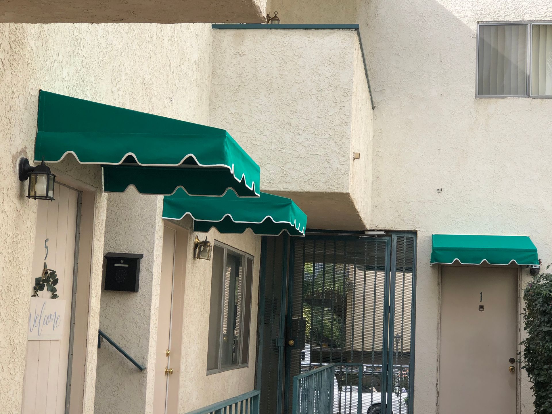 Apartment entrance with green awnings, a gated doorway, and beige stucco walls.