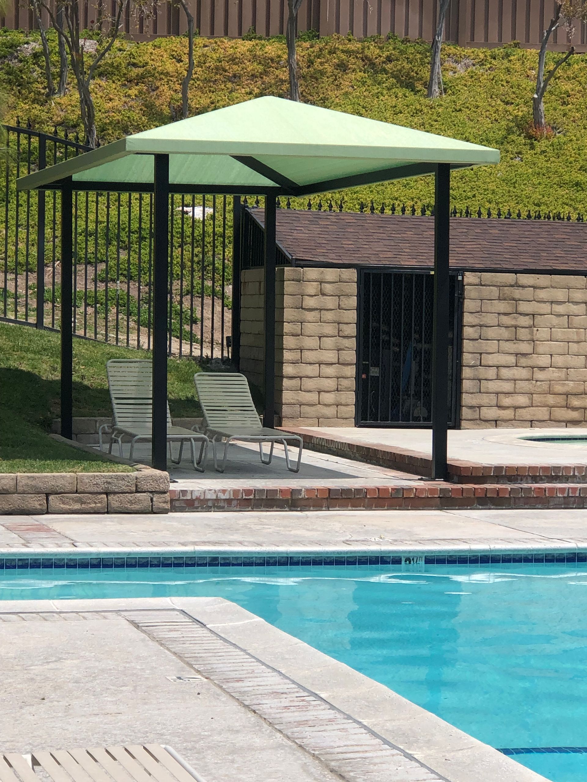 Poolside gazebo with green canopy beside a turquoise swimming pool and stone wall