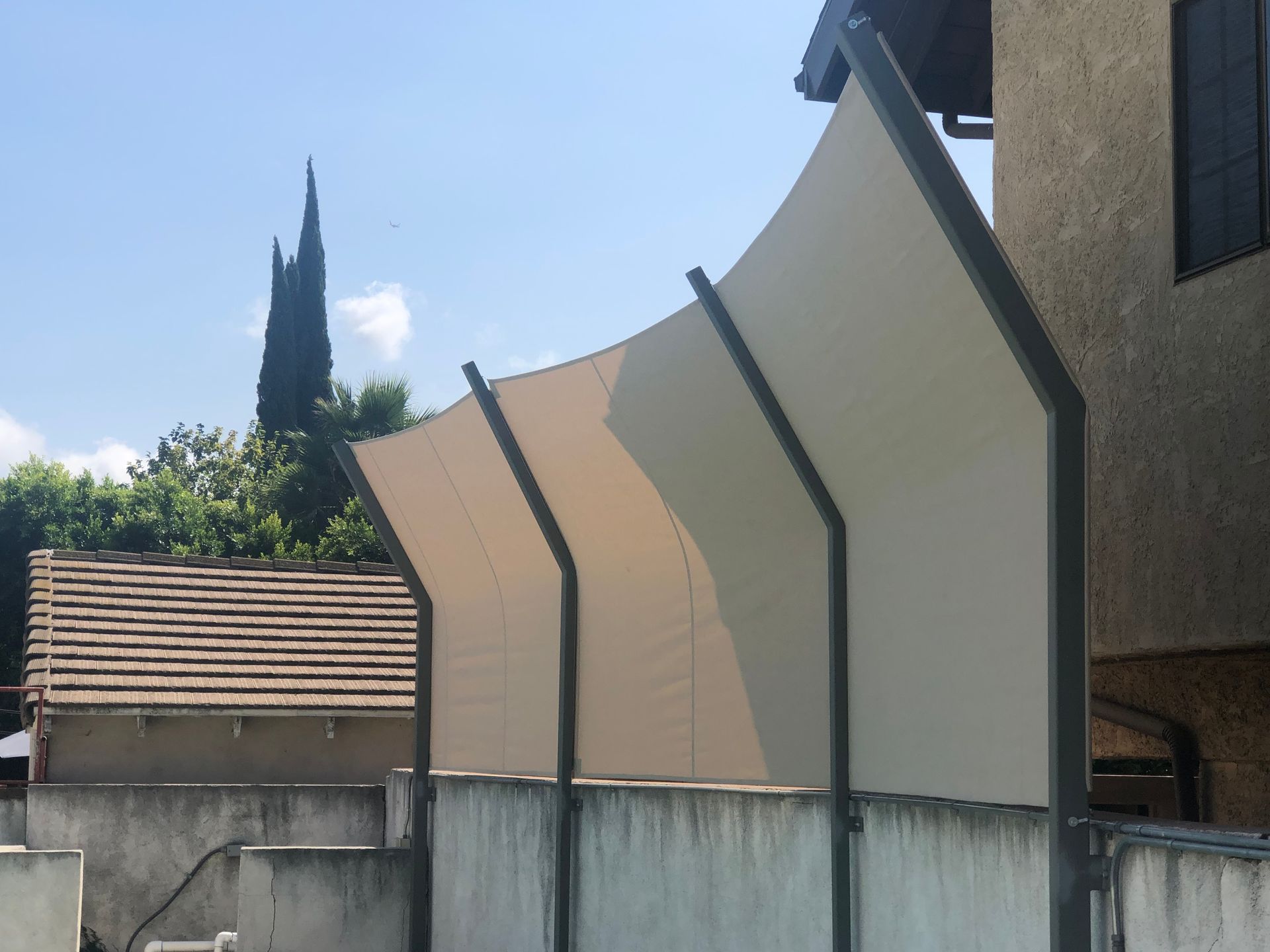 White shade panels mounted along a wall beside a building and fence under a blue sky