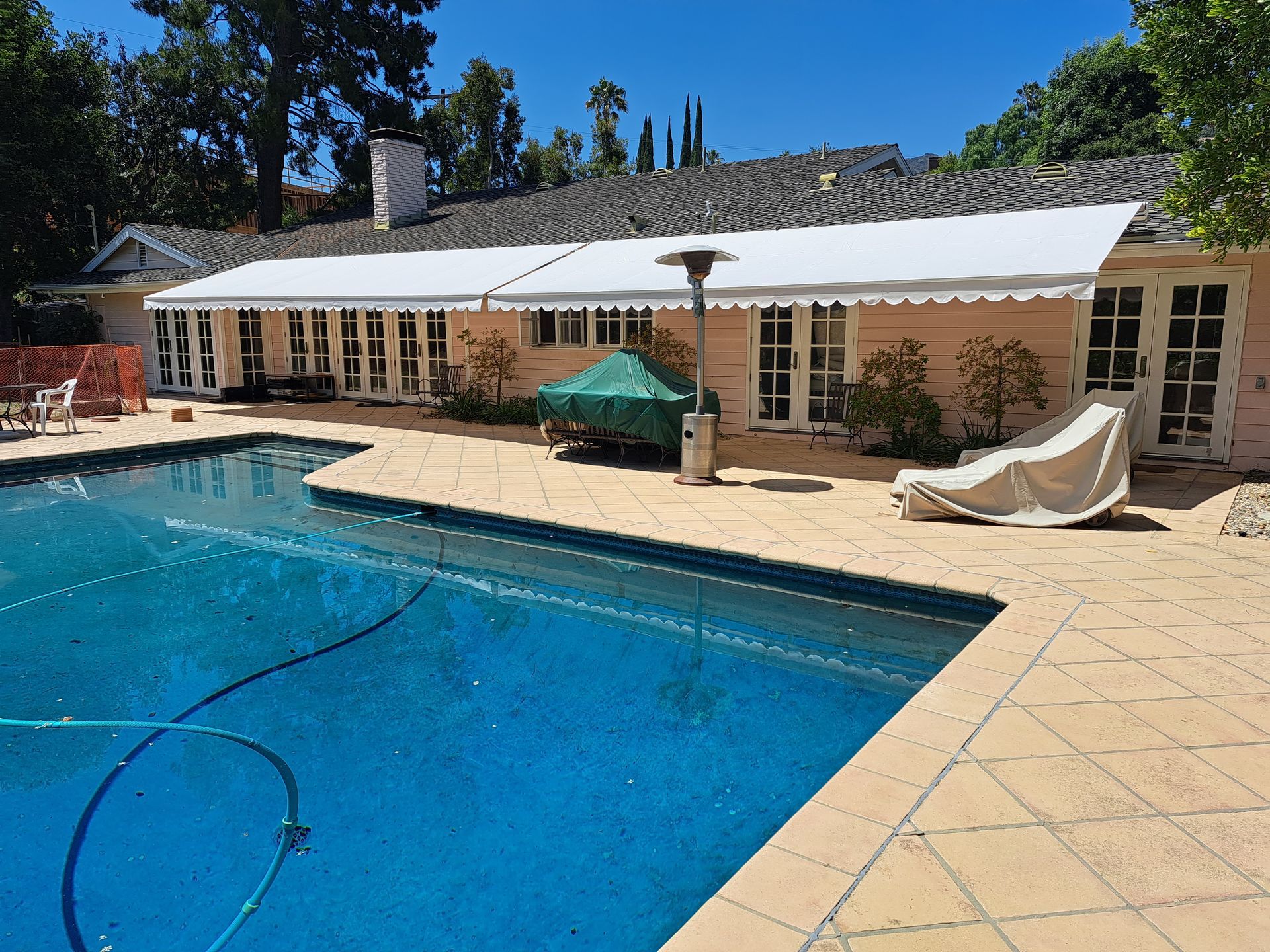 Backyard pool beside a beige house with lounge chairs and a clear blue sky.