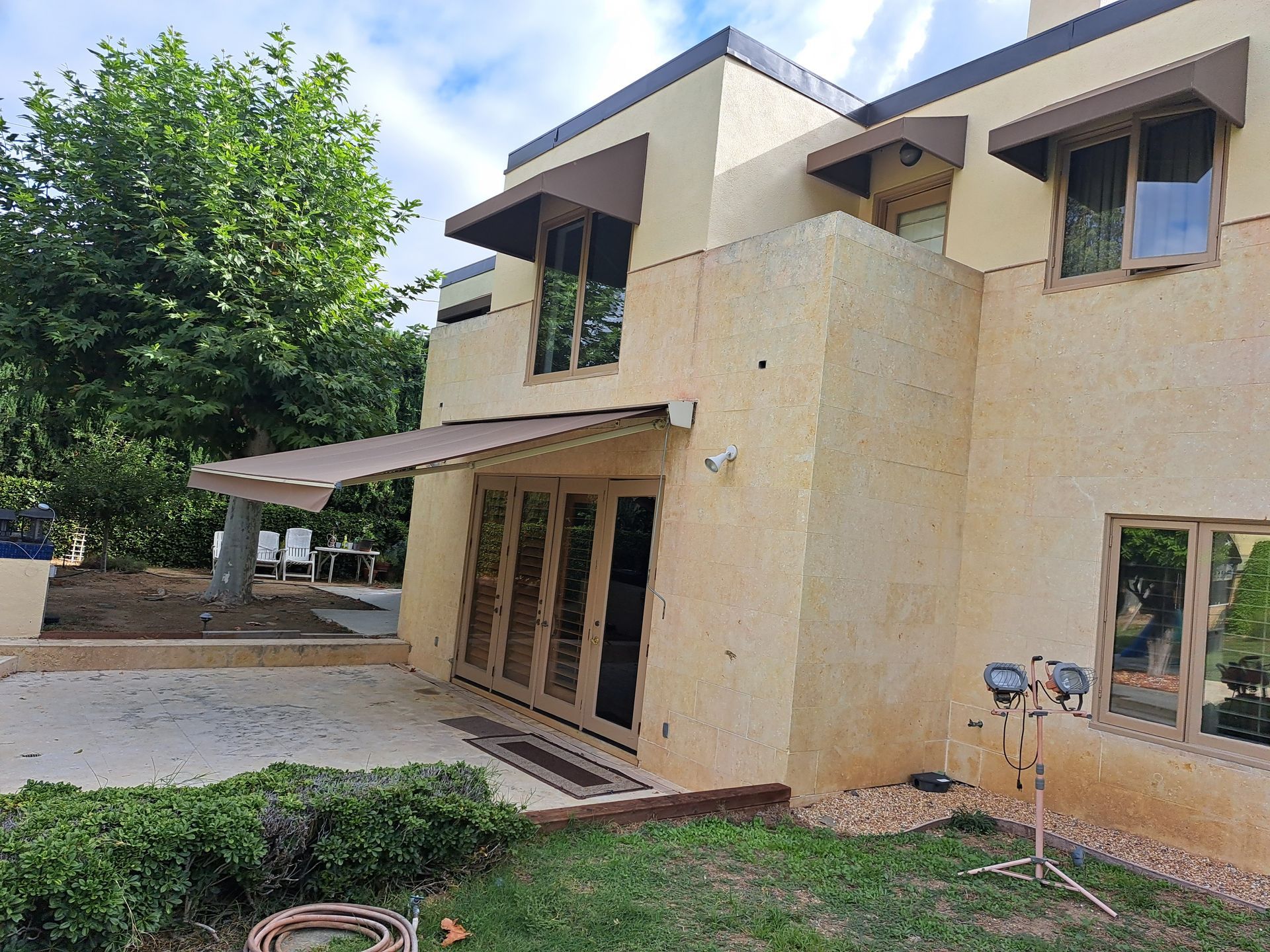 Modern beige two-story house with large windows, covered patio, and landscaped yard
