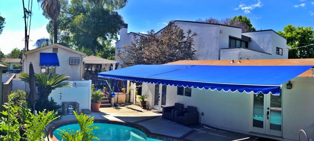 Outdoor patio with a bright blue awning beside white buildings and trees in sunlight