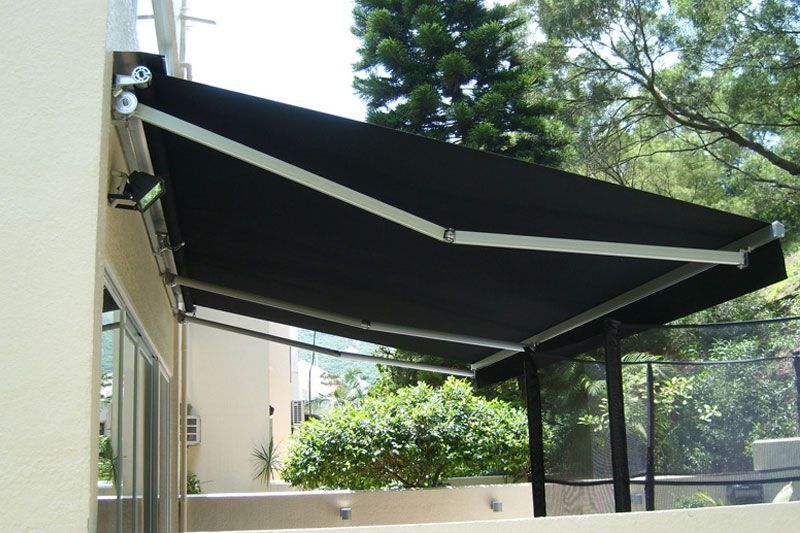 Black retractable awning over a patio beside a house, with trees in the background
