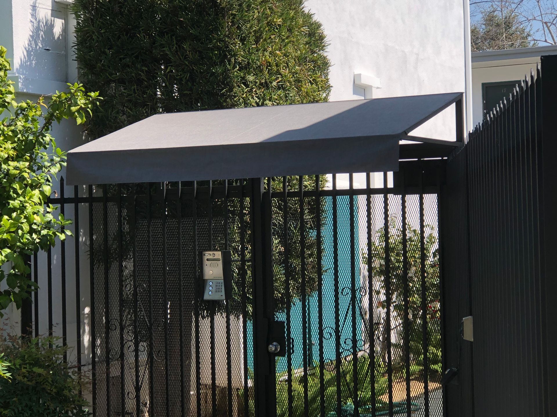 Black metal gate with a gray canopy beside a white building and greenery