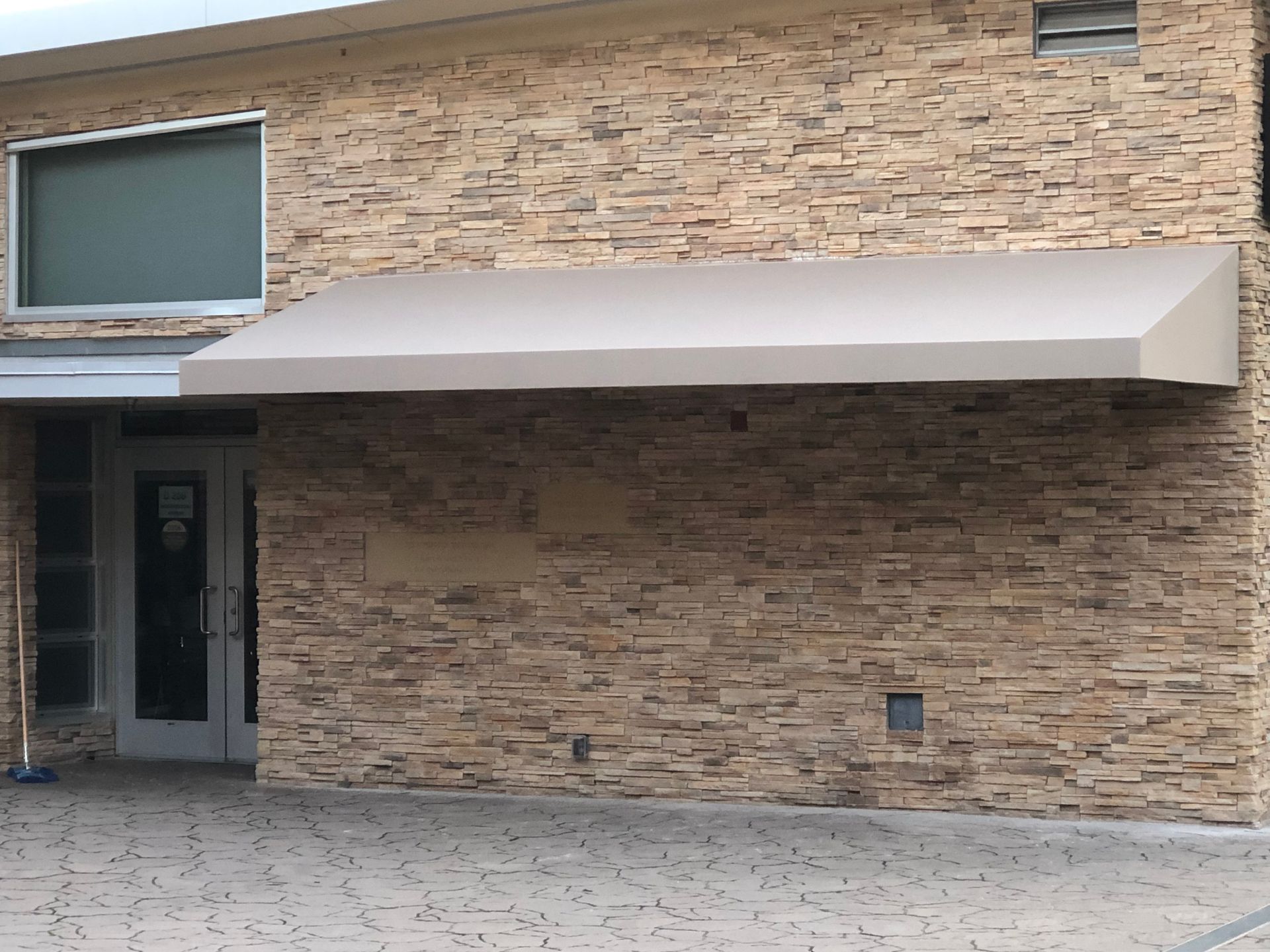 Building entrance with beige brick wall and a large tan awning over the door