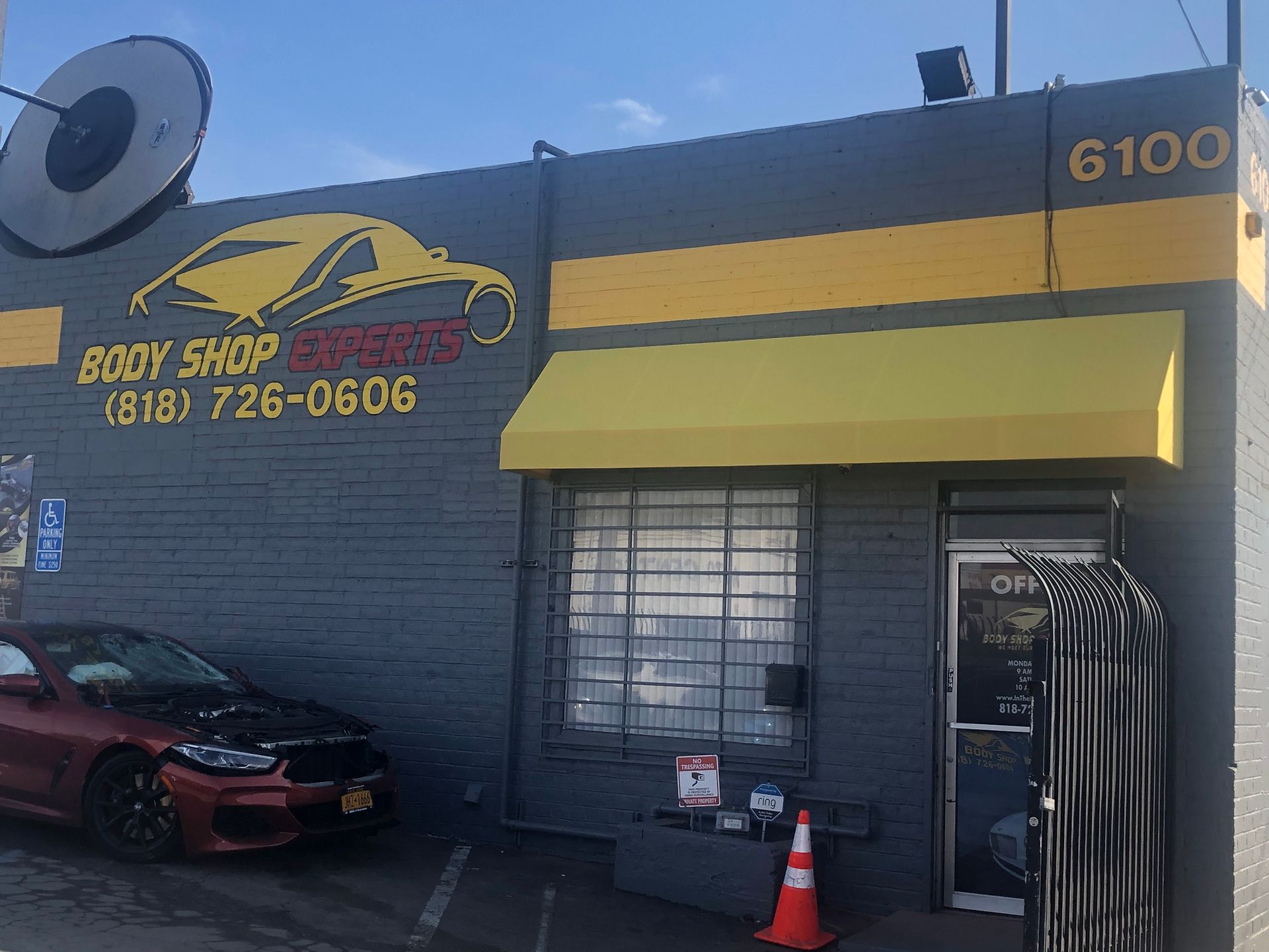 Body shop storefront with yellow awning, car parked outside, and shop number 6100 on the wall