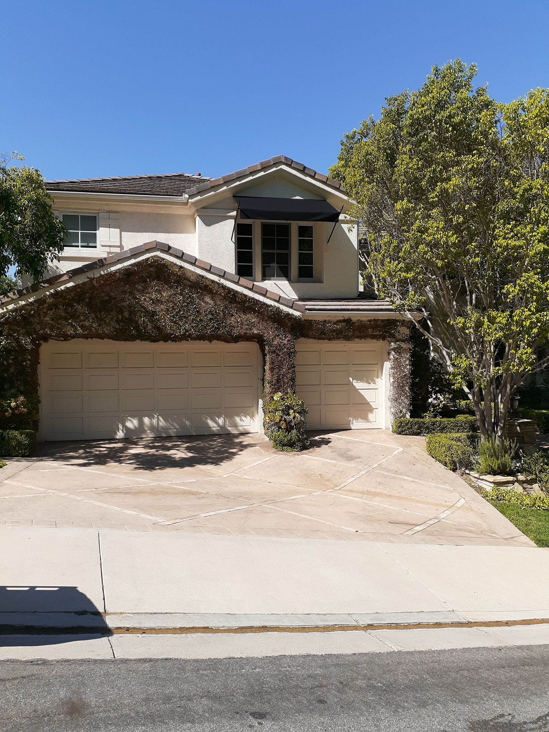 Two-story suburban house with a two-car garage and a tree in the front yard.