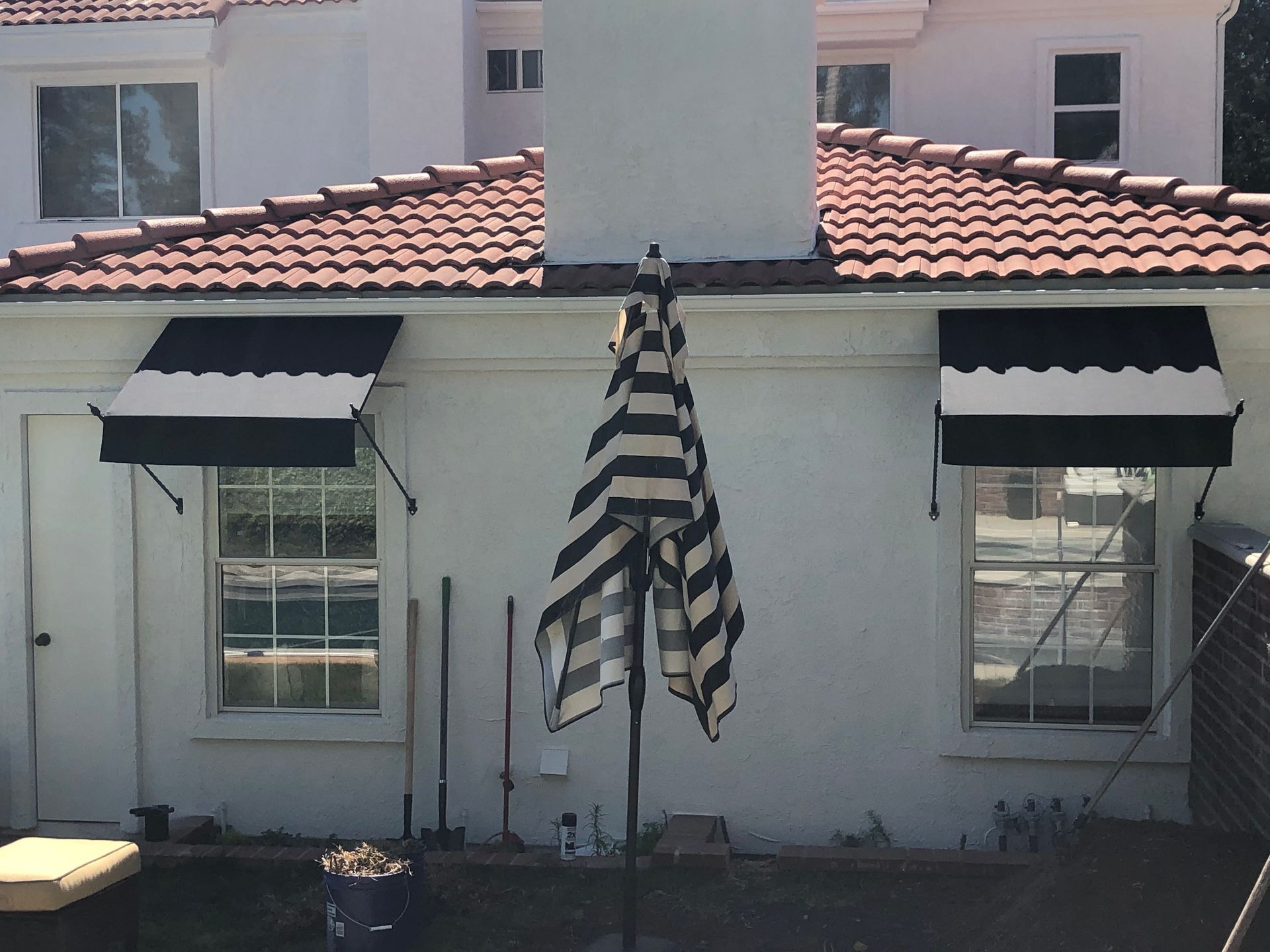 Patio with black-and-white striped umbrella in front of a white house with black window awnings