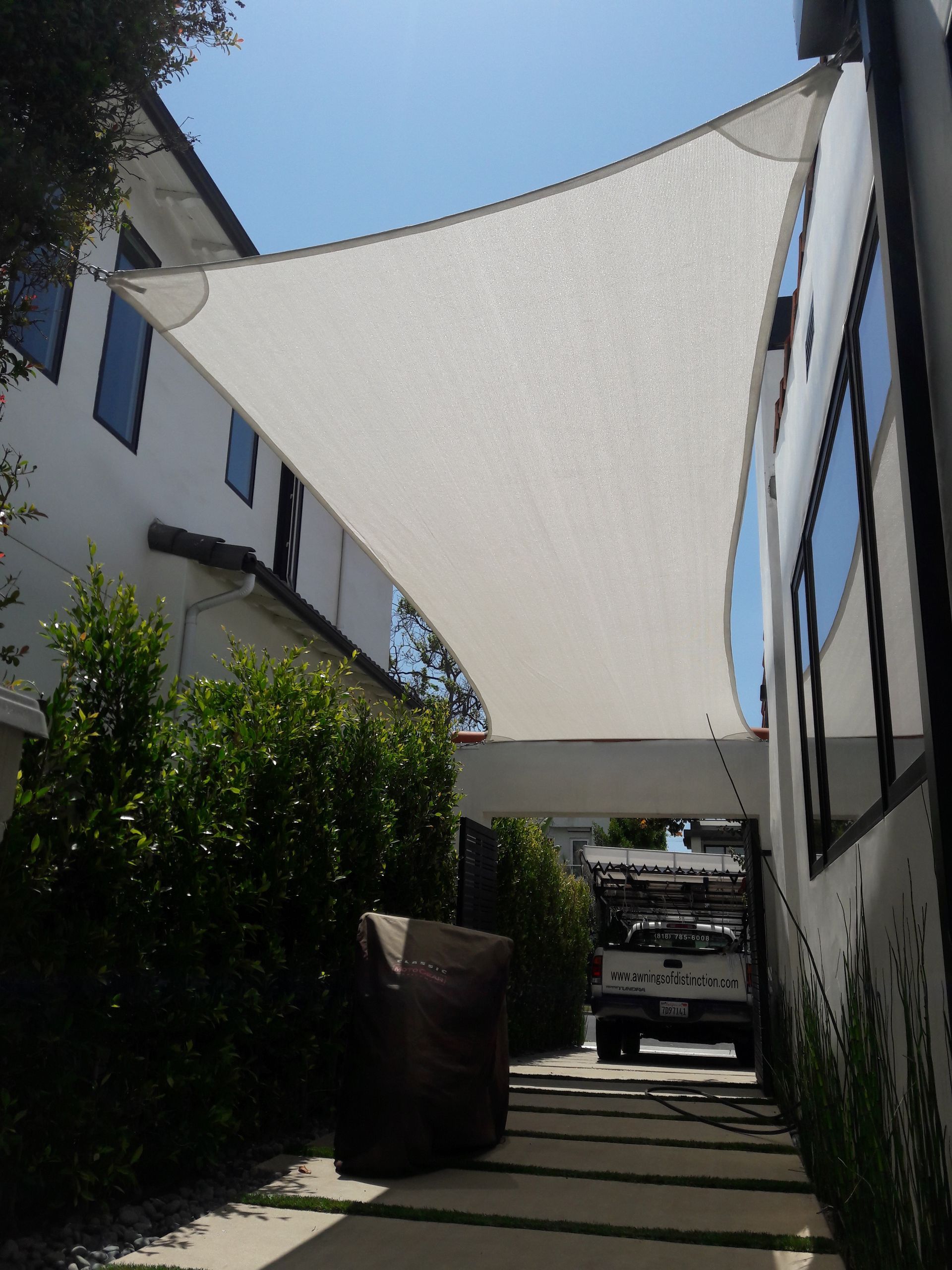 Sunny alleyway between buildings with white shade sails overhead and a parked vehicle at the end.