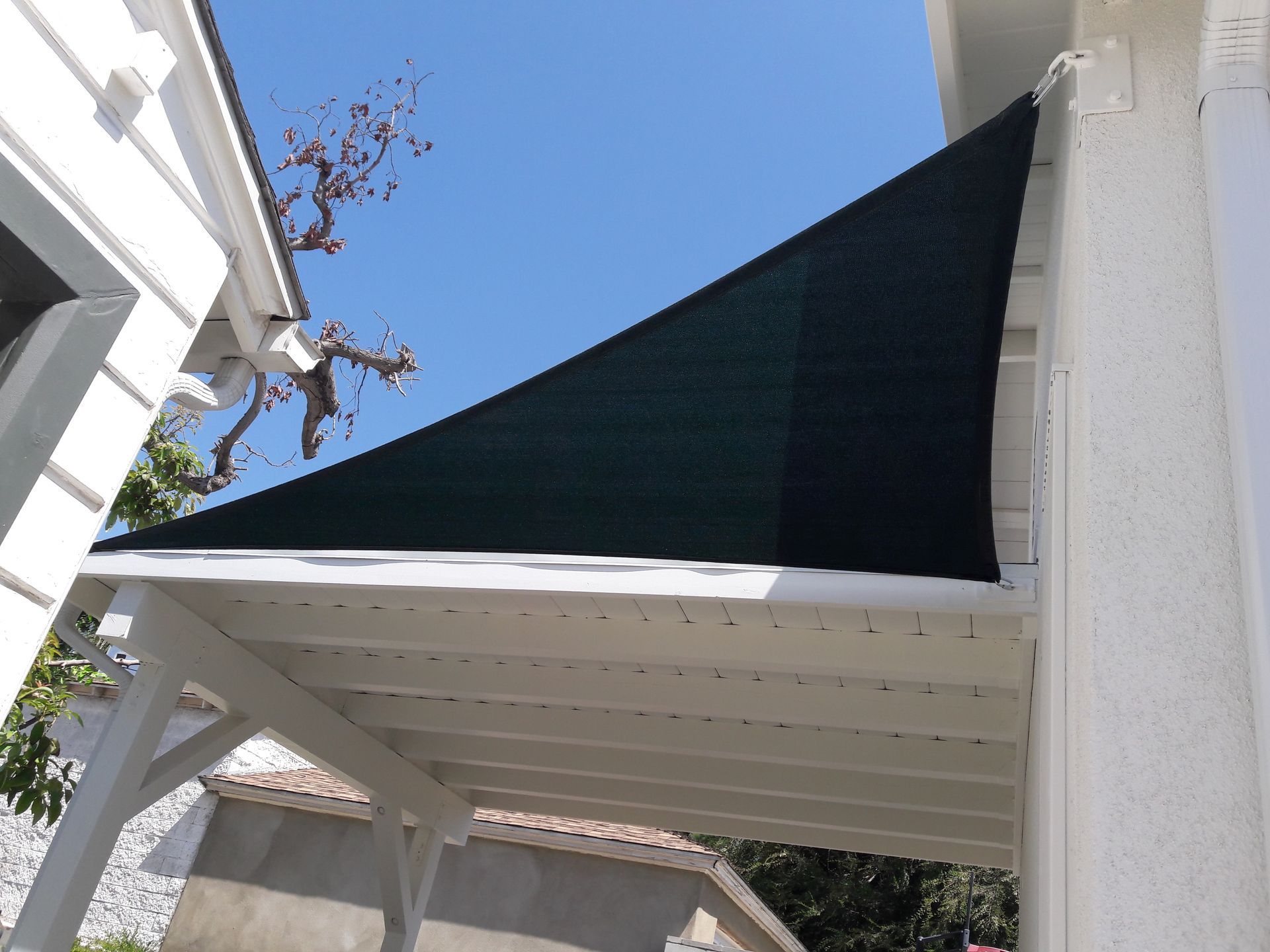 Black triangular shade sail above a white patio roof against a blue sky