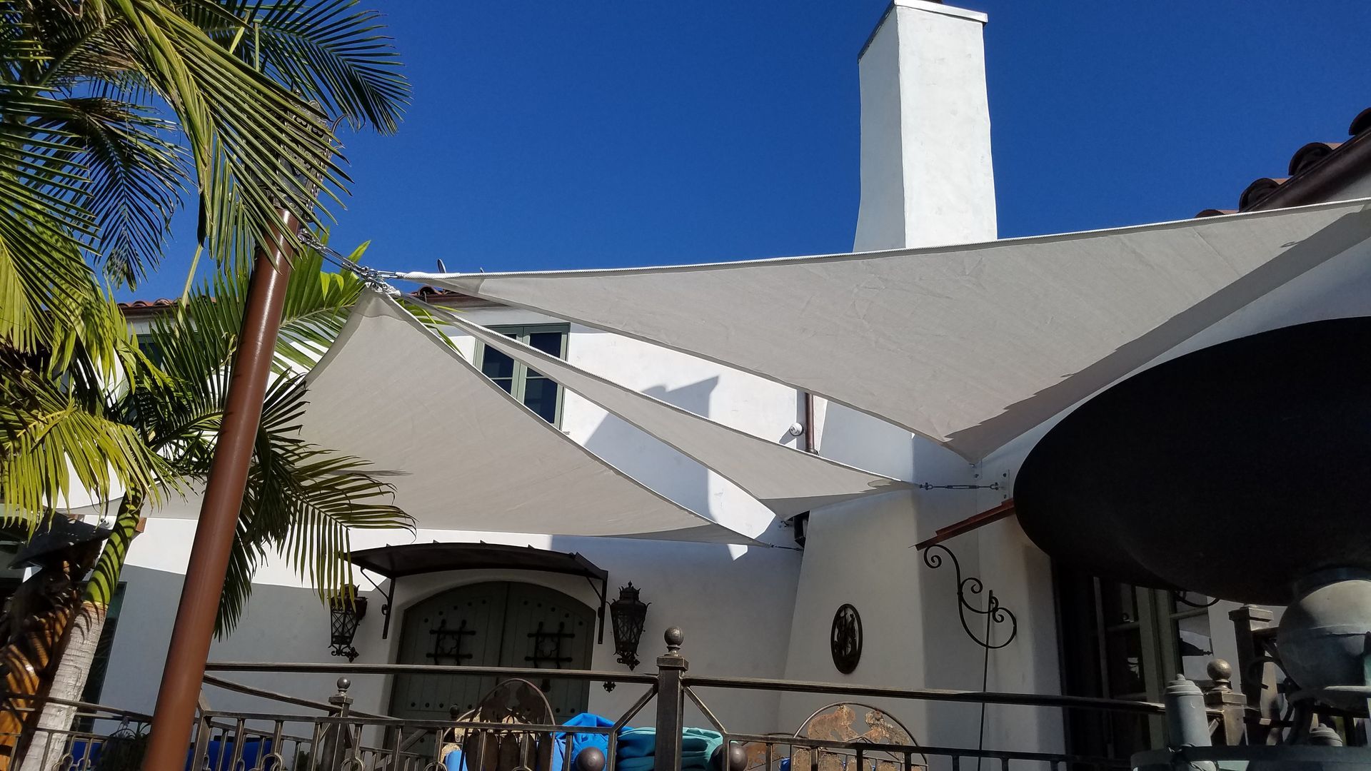 White building with triangular shade sails, blue sky, palm trees, and a covered entrance