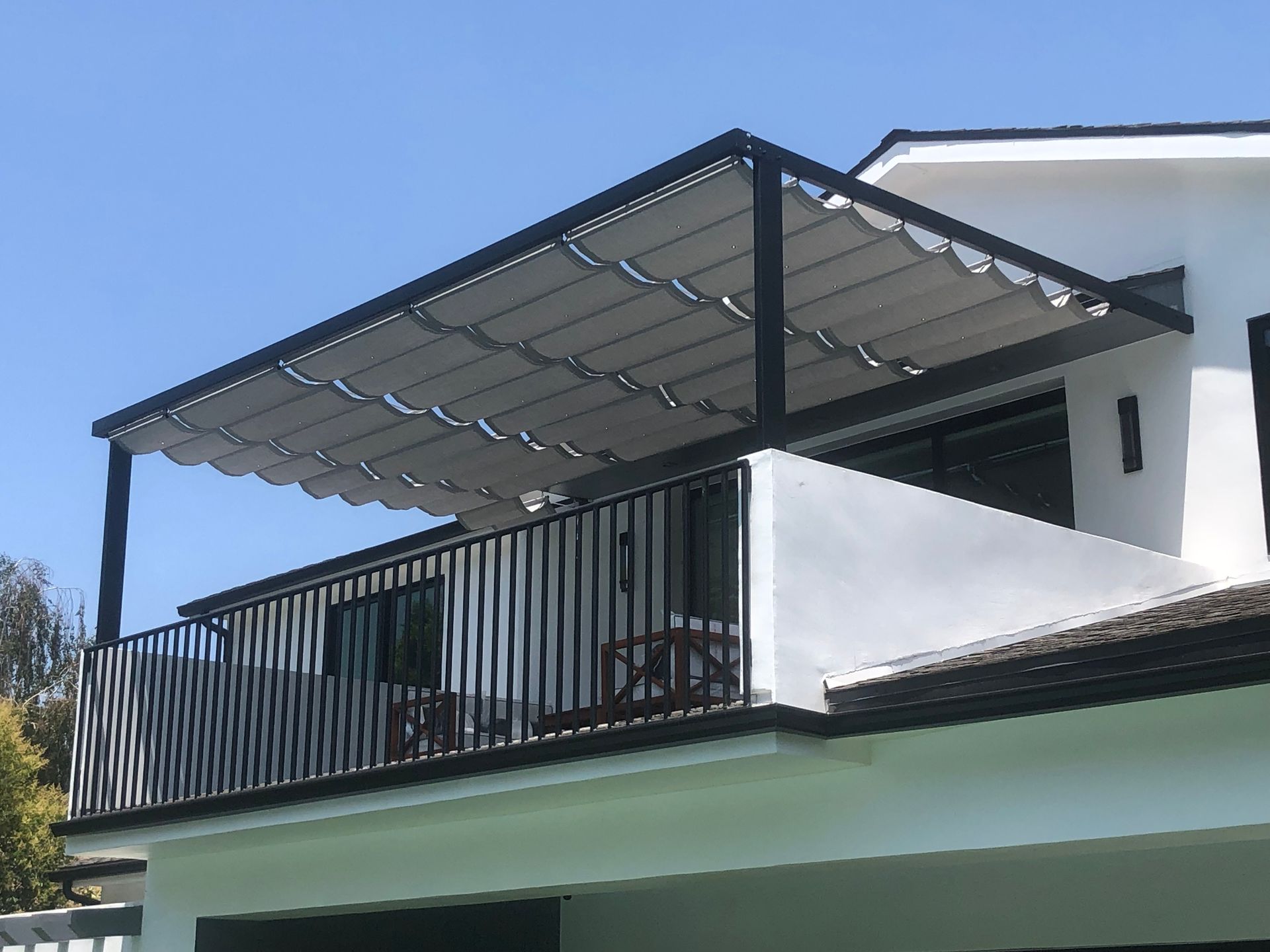 Balcony with black railing and metal awning on a white house under a blue sky