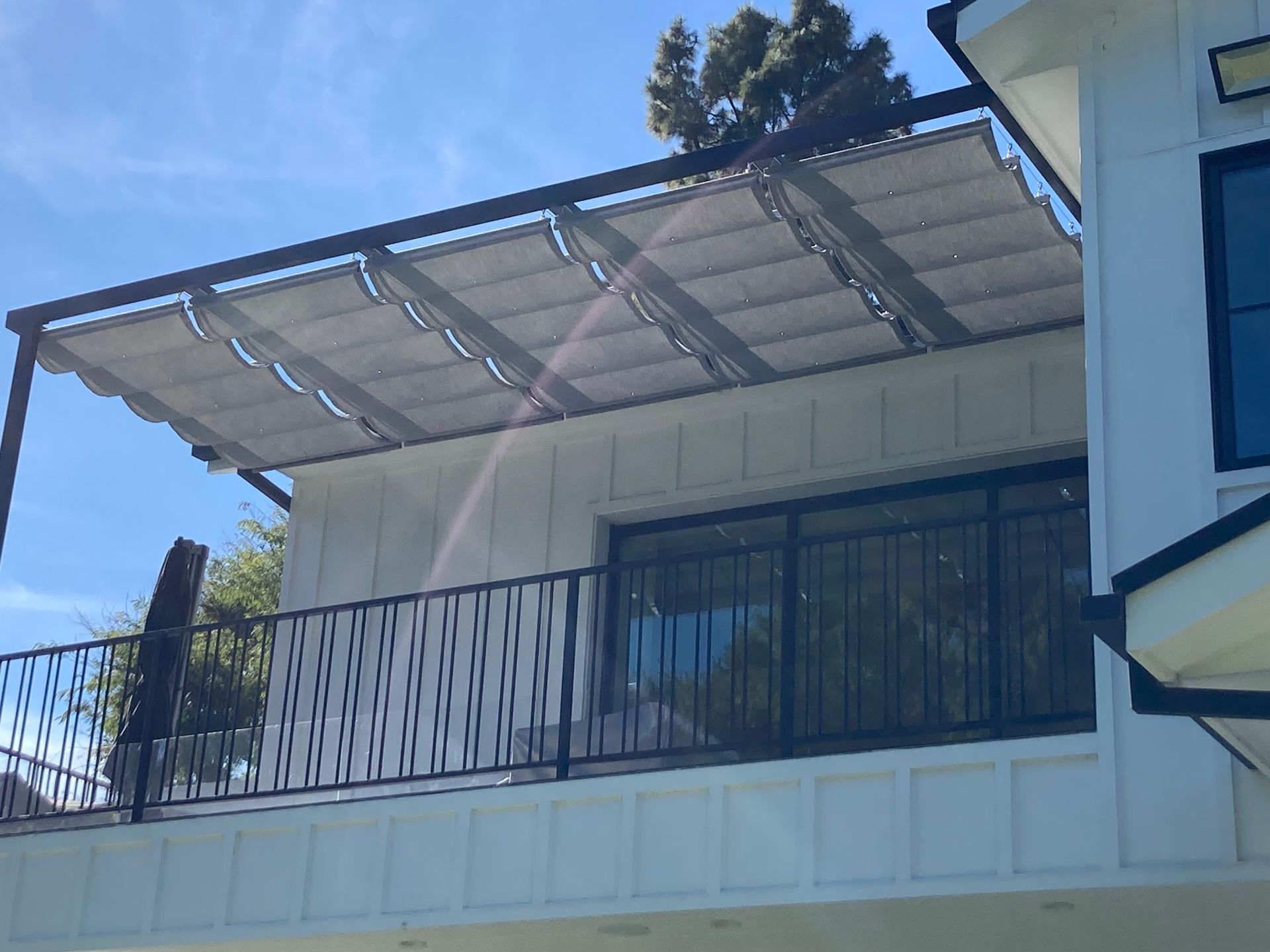 White house balcony with metal railing and a translucent awning under a blue sky
