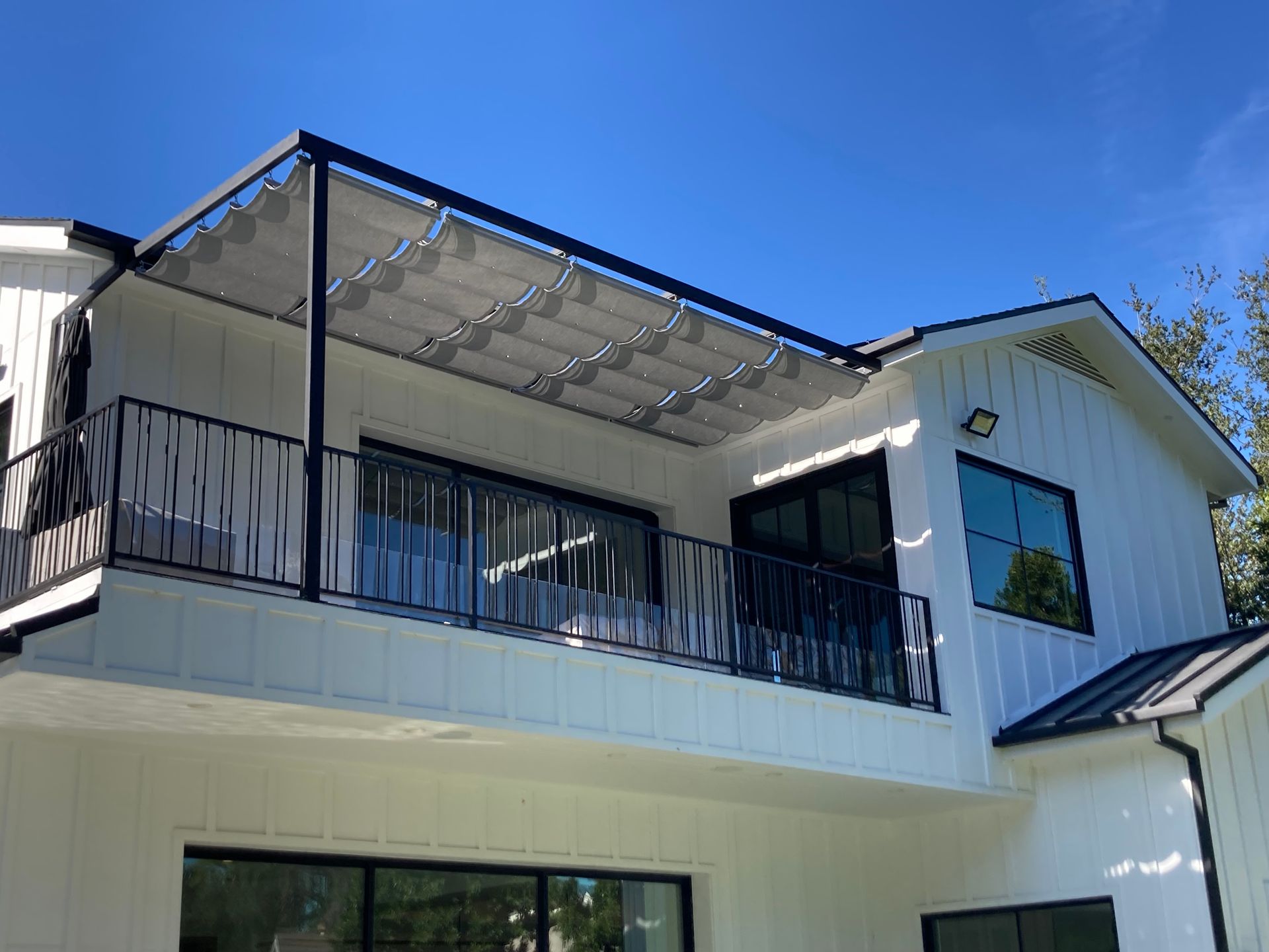 Two-story white house with black balcony railings and a glass awning under a blue sky