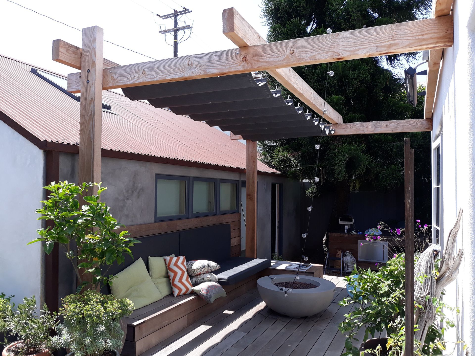 Backyard patio with wooden pergola, bench seating, and round fire pit beside a house