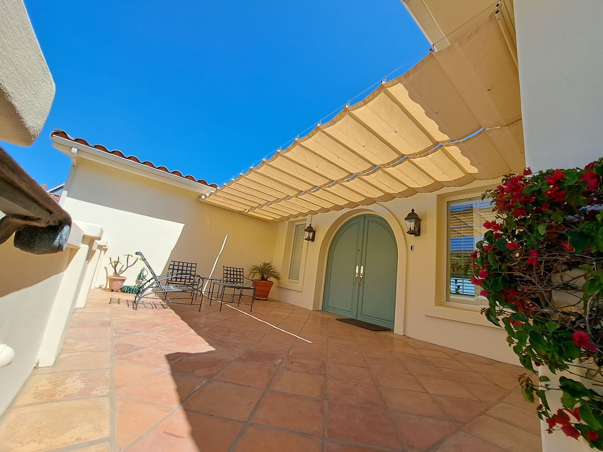 Sunlit courtyard patio with terracotta tiles, arched doorway, pergola shade, and flowering bougainvillea.